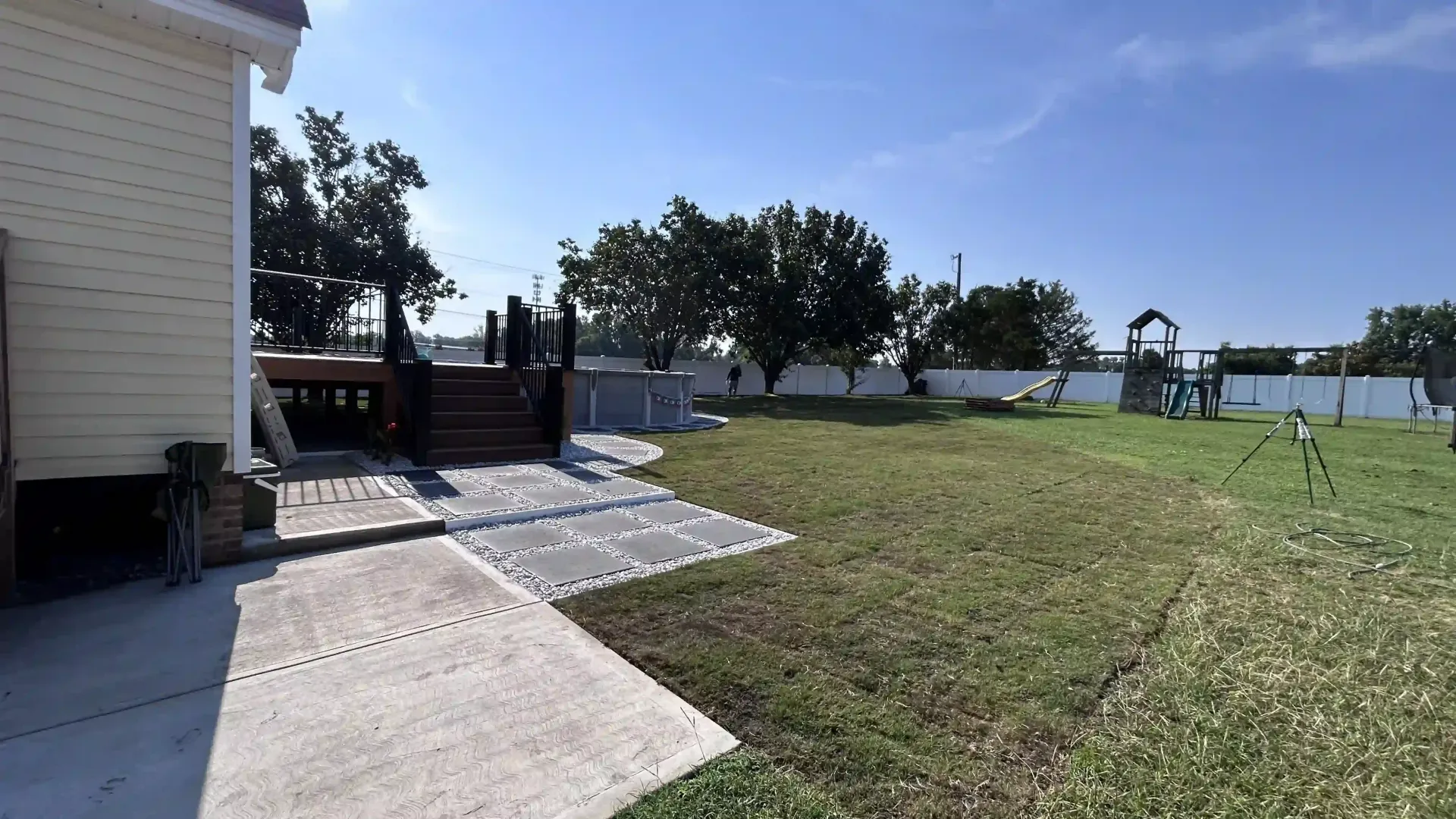House patio with concrete walkway leading to a grassy yard, trees, and a waterfront view