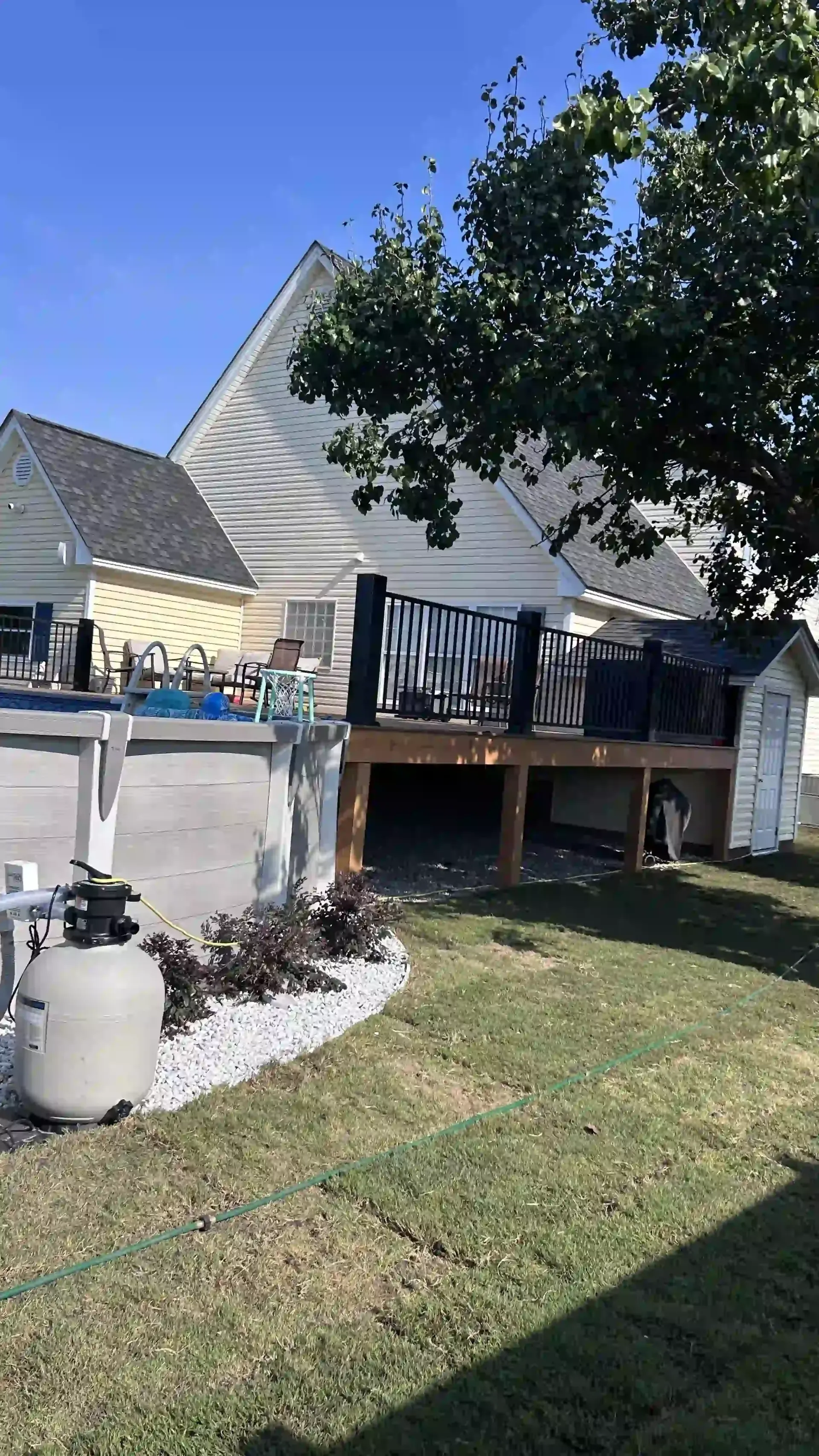 Backyard deck with a gray A-frame house, grill area, and a tree casting shade over the lawn