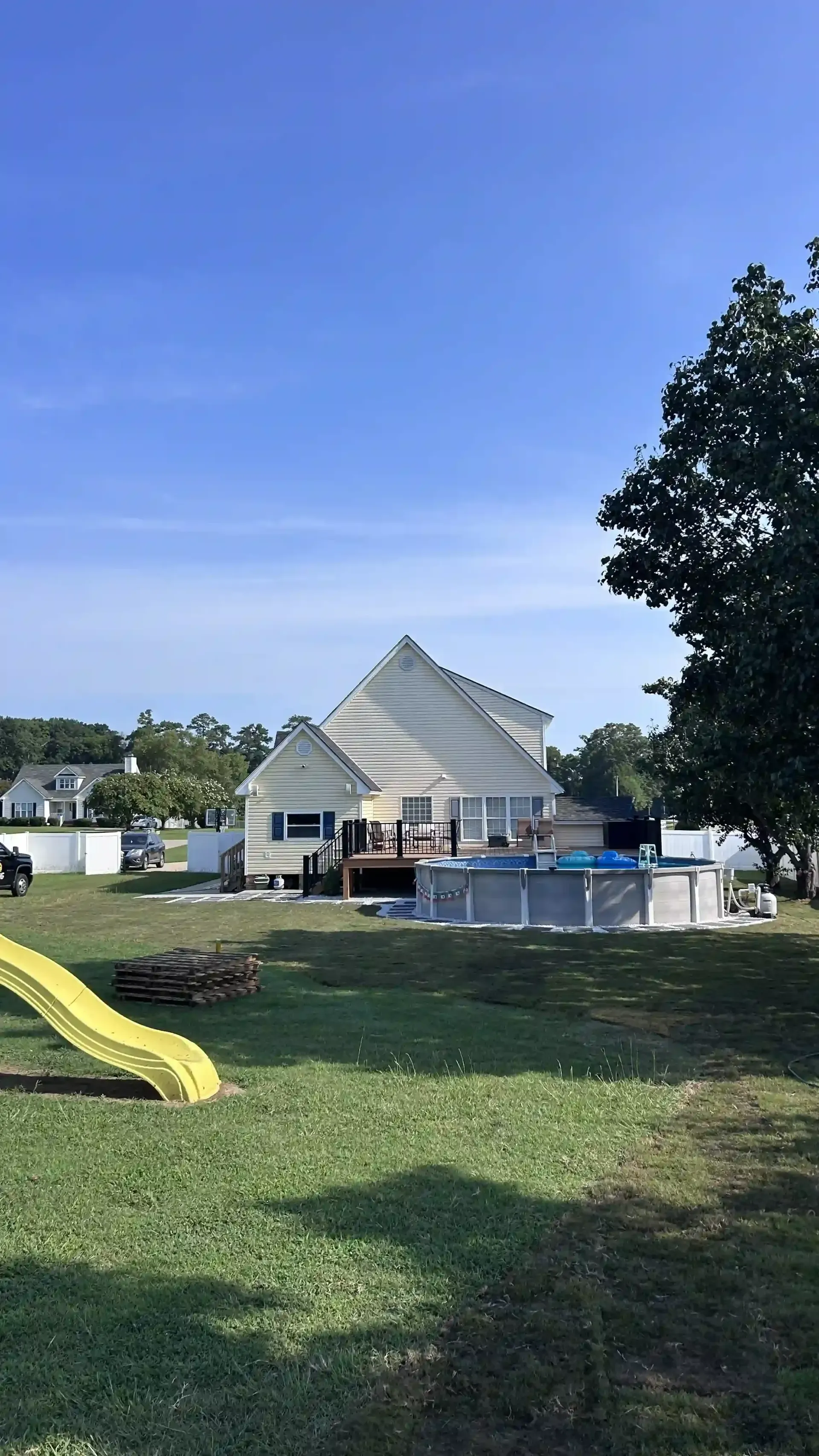 Park with a yellow slide, grassy lawn, and a white pavilion under a clear blue sky.