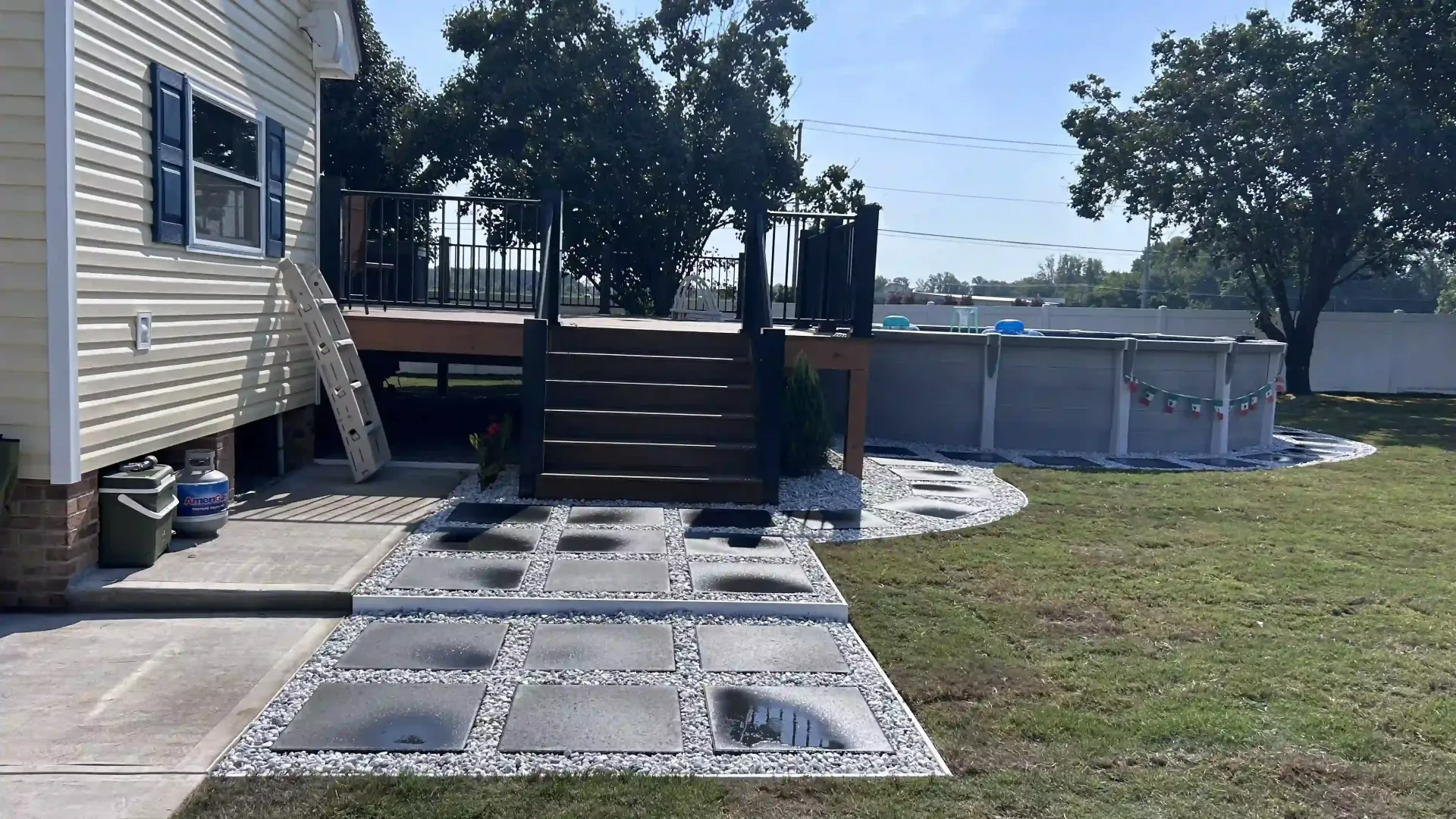Backyard deck beside a house with concrete pavers and grassy yard near a fence and trees
