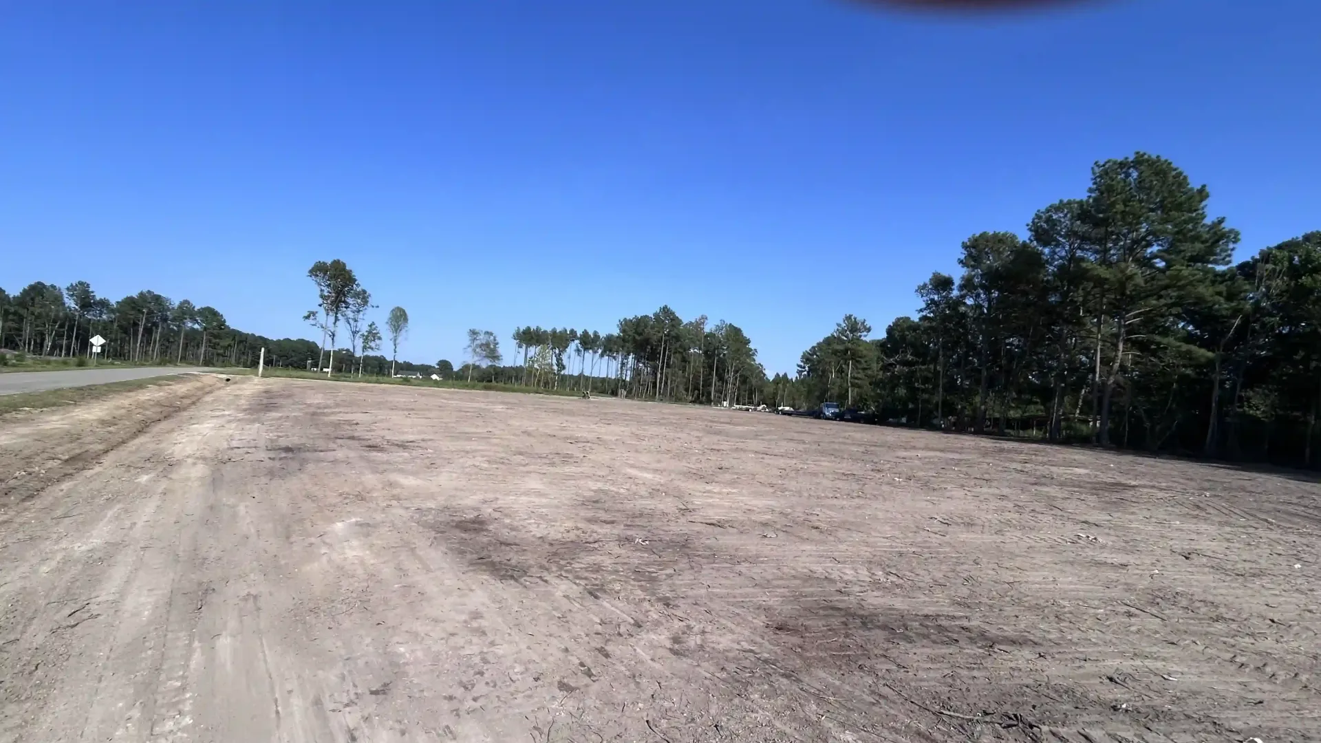 Wide dirt clearing beside trees under a bright blue sky.