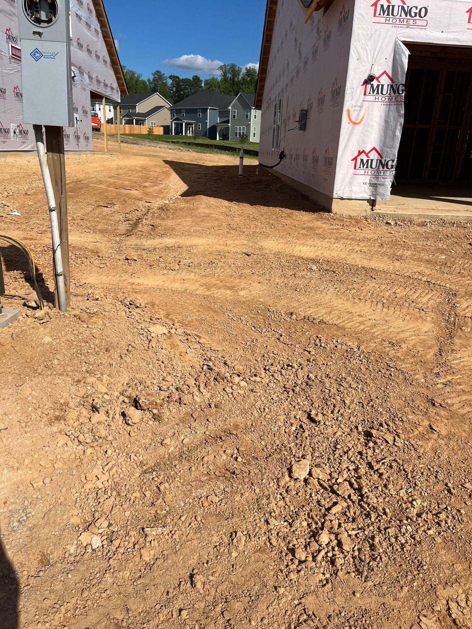 Construction site with a dirt yard between two buildings, overhead power lines.