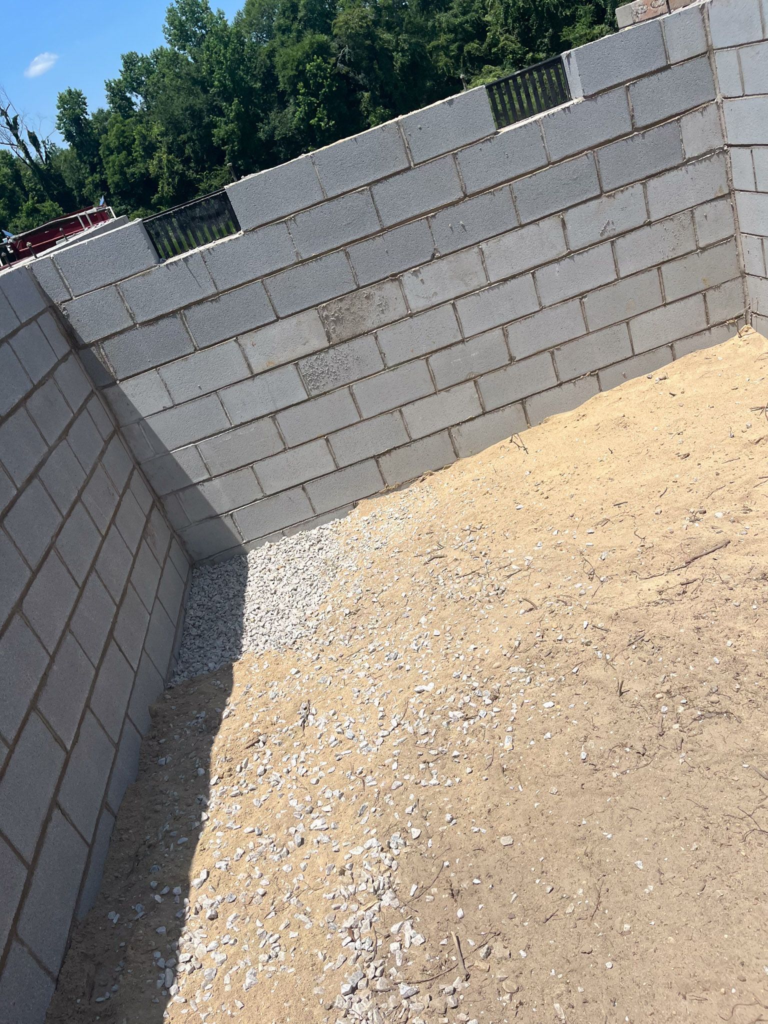 Gray concrete block walls enclosing a sand and gravel-covered space, likely a foundation.