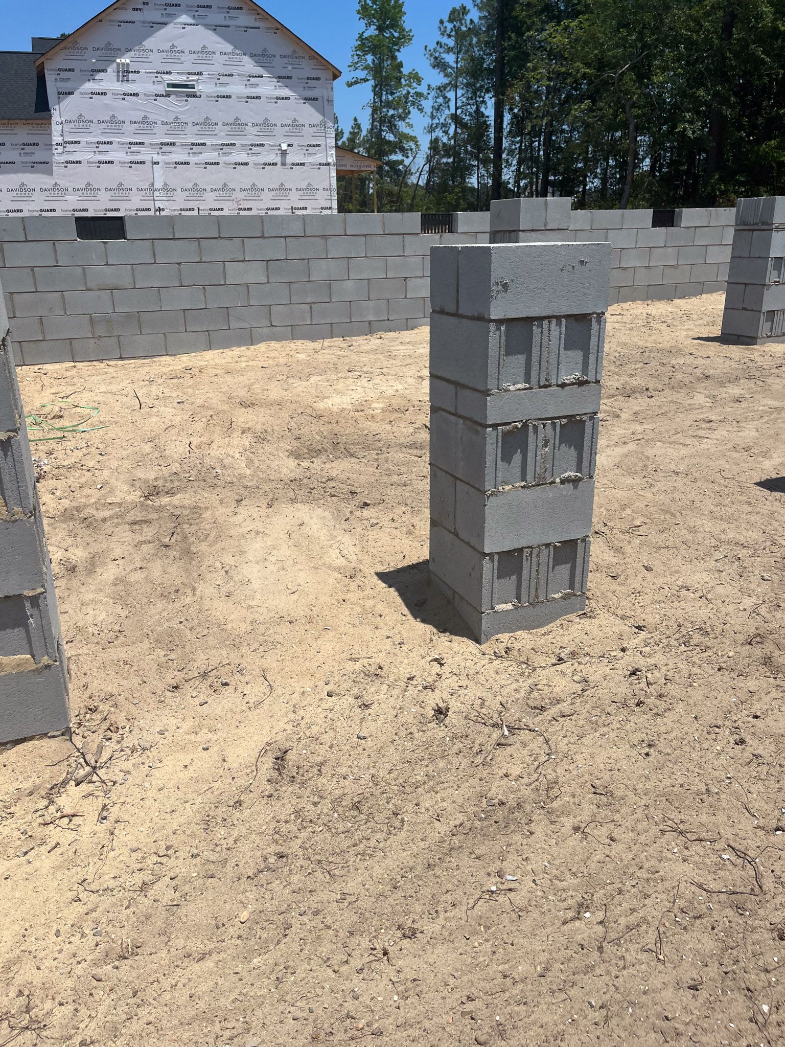 Construction site with gray cinder block foundation walls and supporting pillars on a dirt ground.