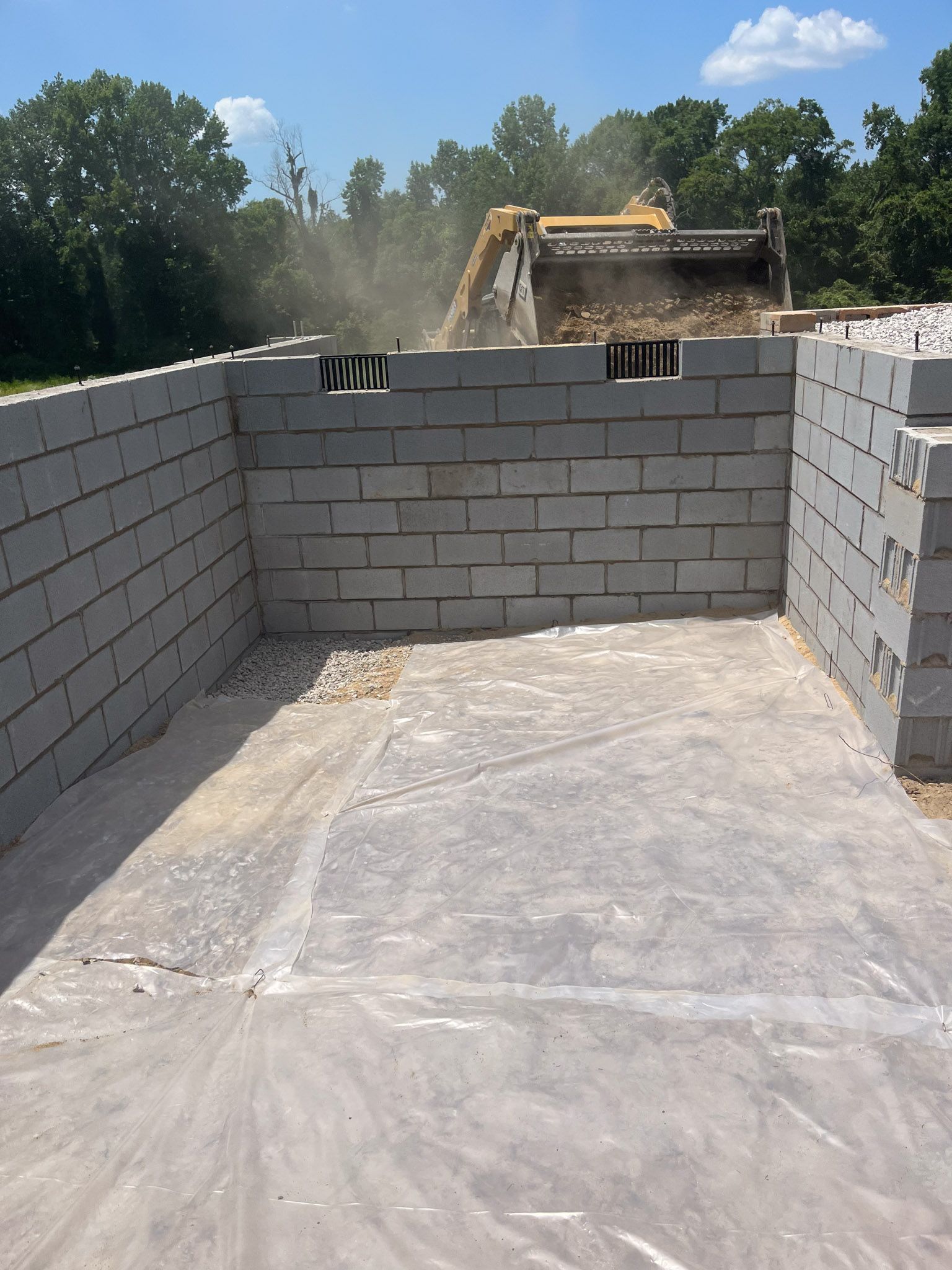 A construction site with an excavator filling a bin made of gray concrete blocks.