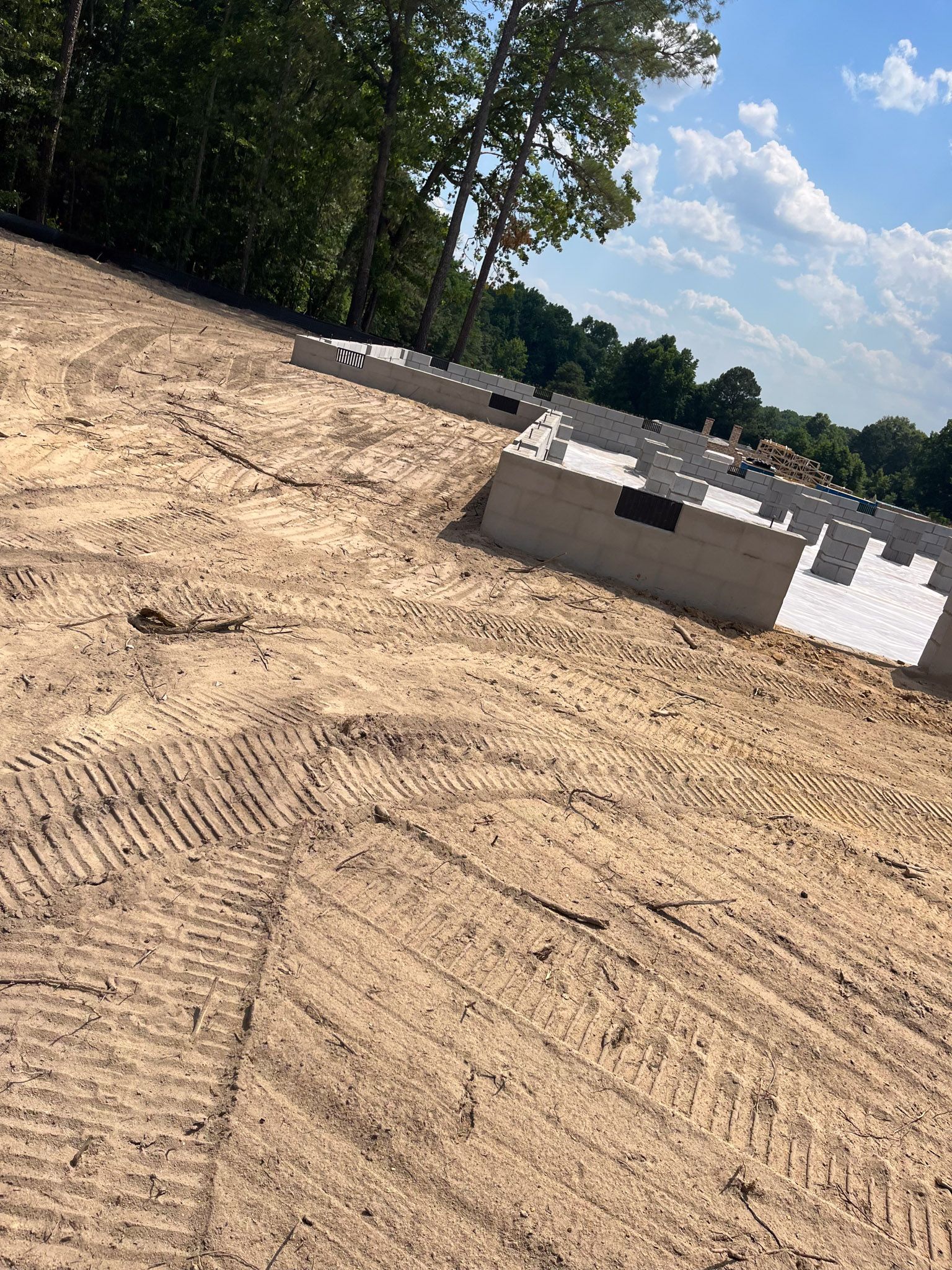 Construction site with a concrete foundation on a dirt lot, trees and blue sky background.