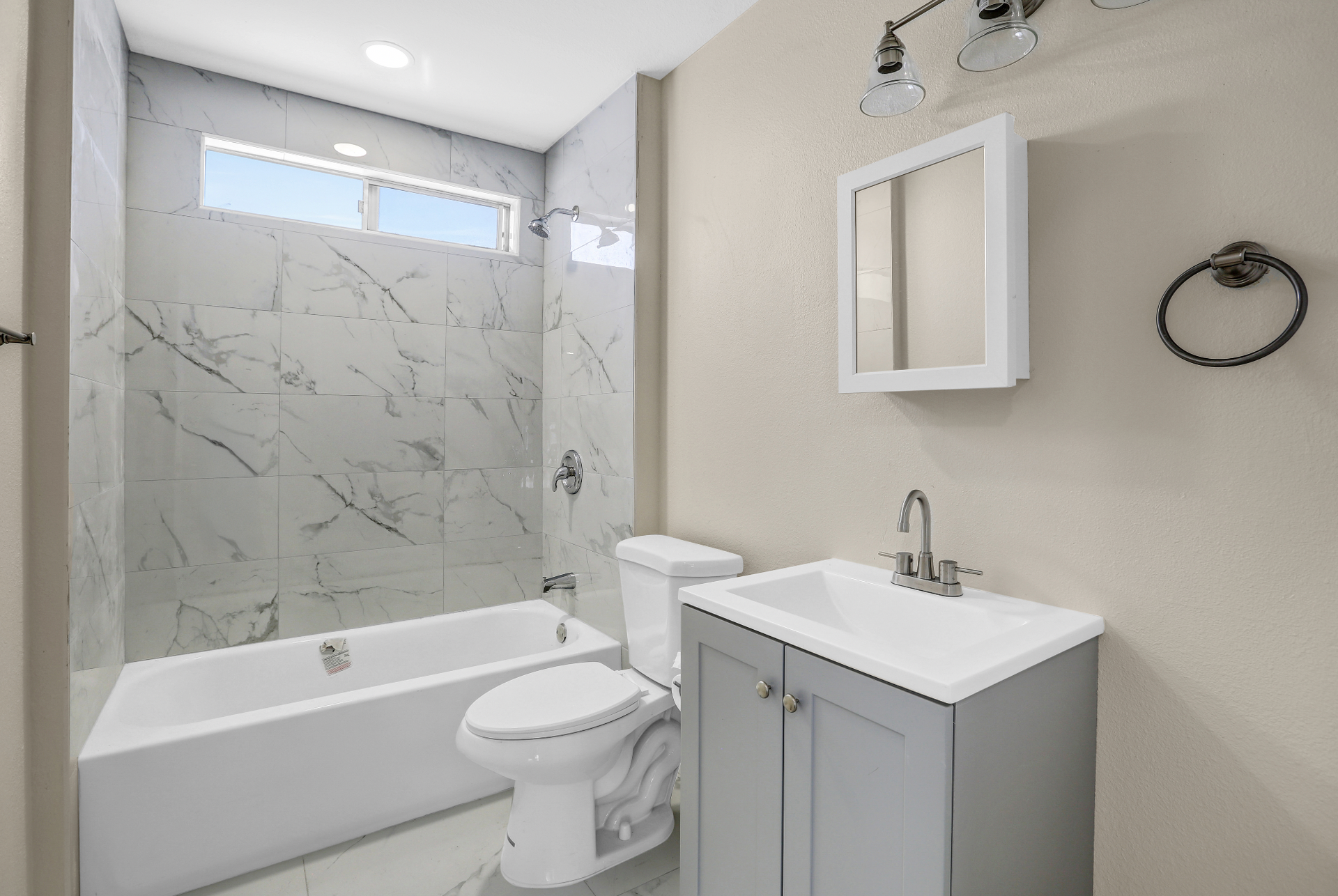 Bathroom with marble tile, a bathtub, a toilet, a vanity, and a mirror.