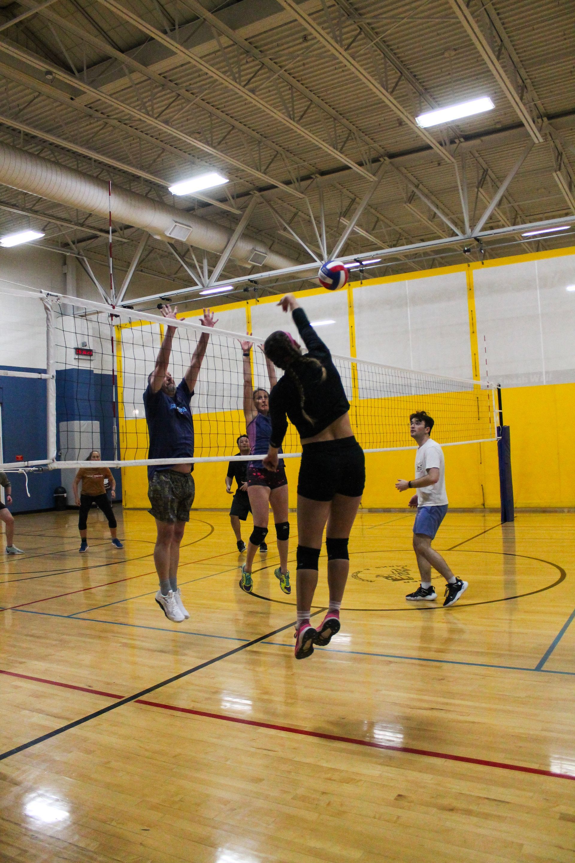 People playing a volleyball game in an indoor gym, focusing on an active jump-set at the net.