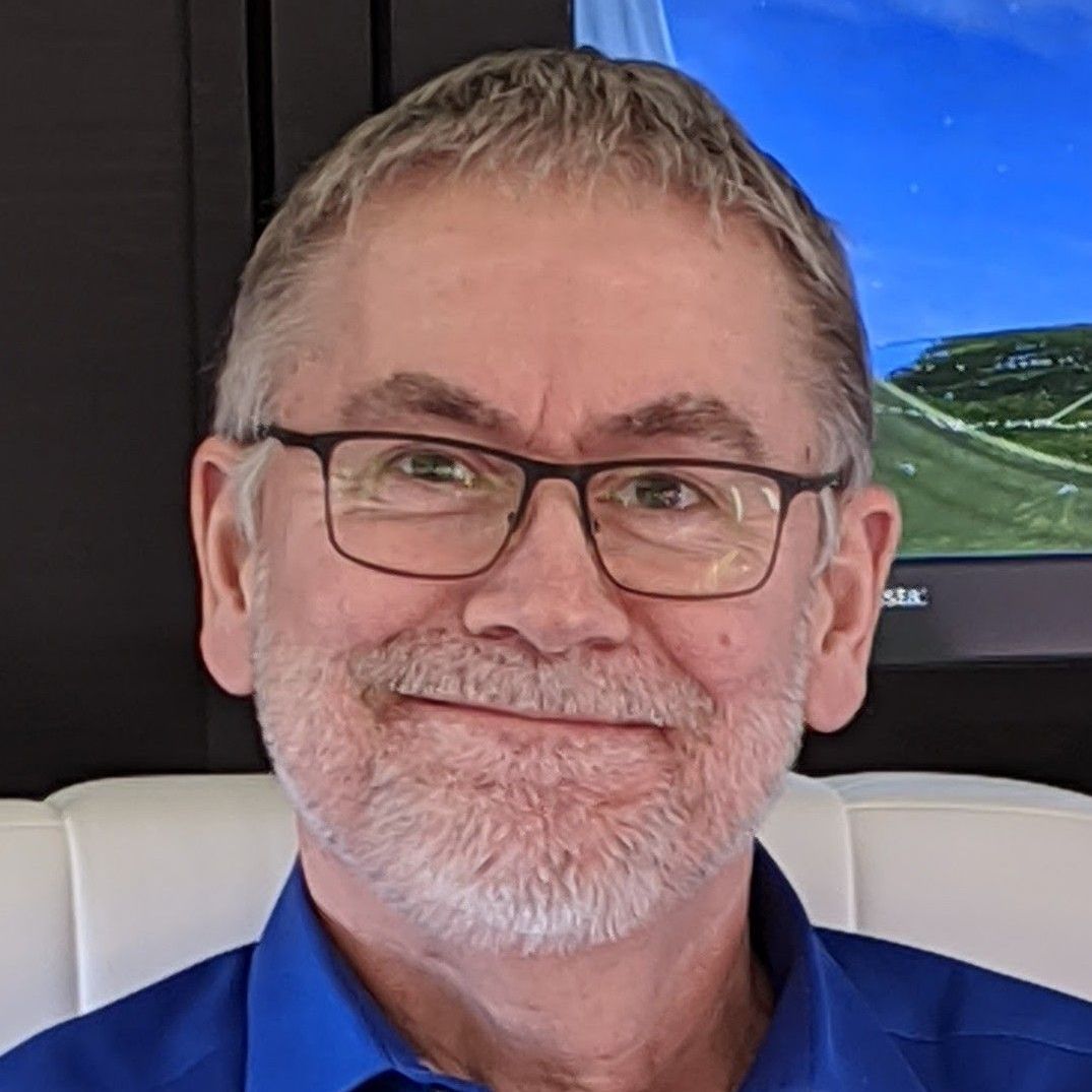 A man with glasses and a beard is smiling in front of a television.