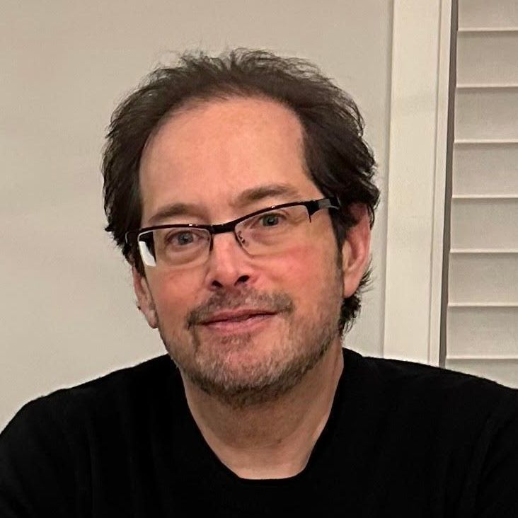 A man wearing glasses and a black shirt is smiling for the camera.