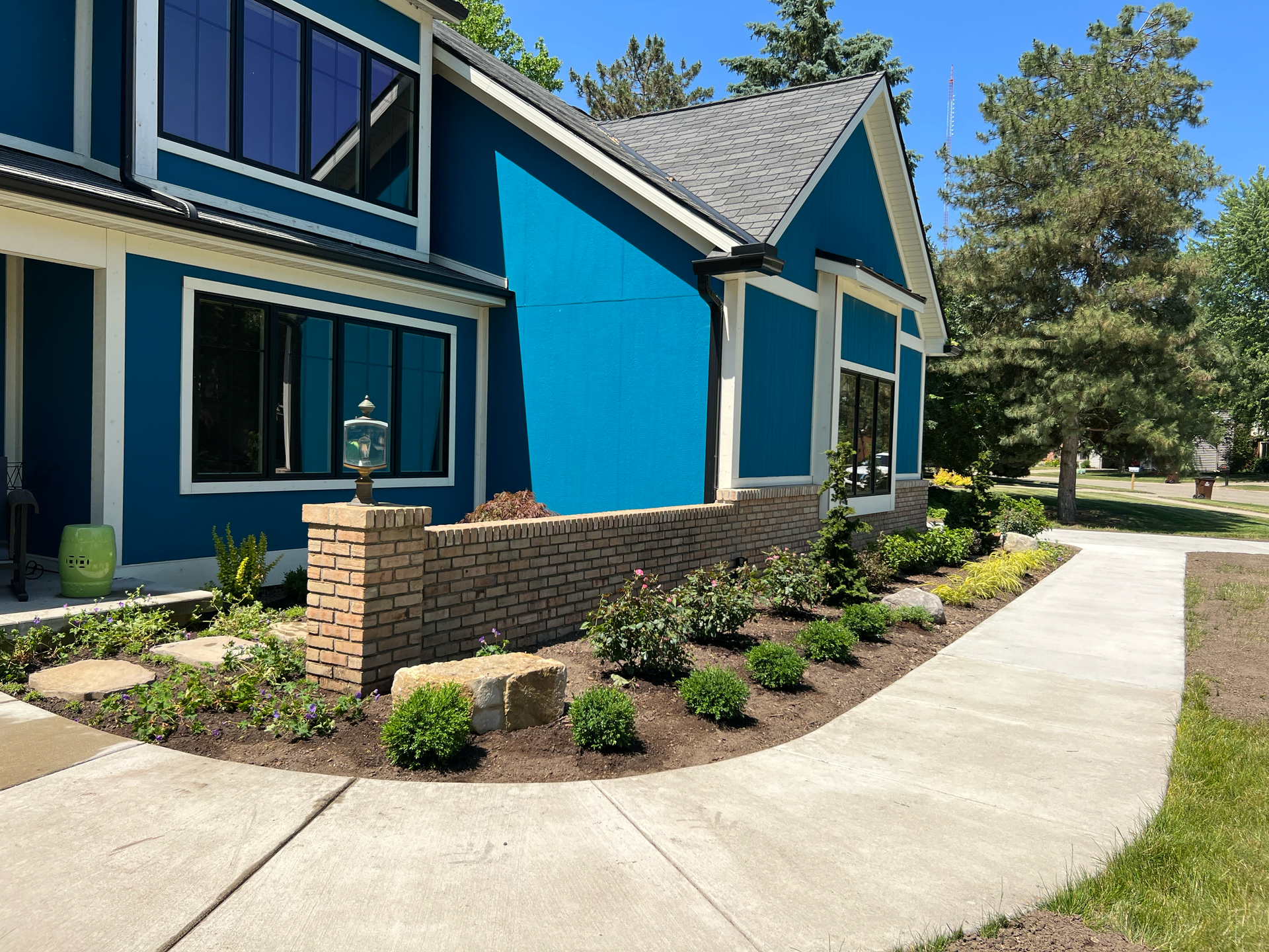 Blue house with brick wall, windows, and landscaped walkway.