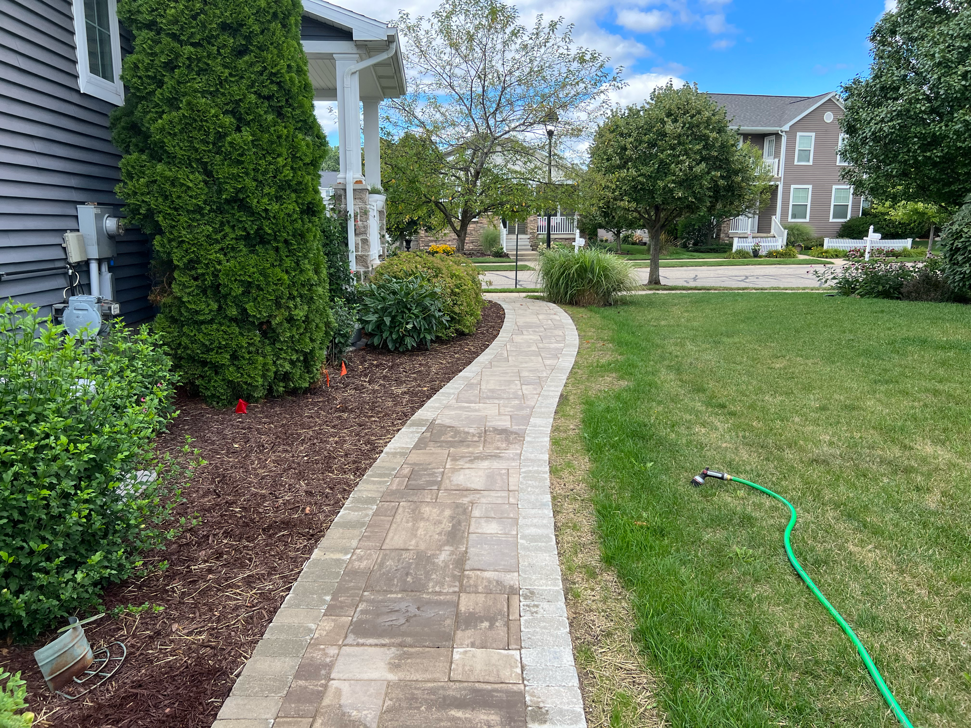 Brick pathway leading to a house, flanked by green lawn and landscaped beds.