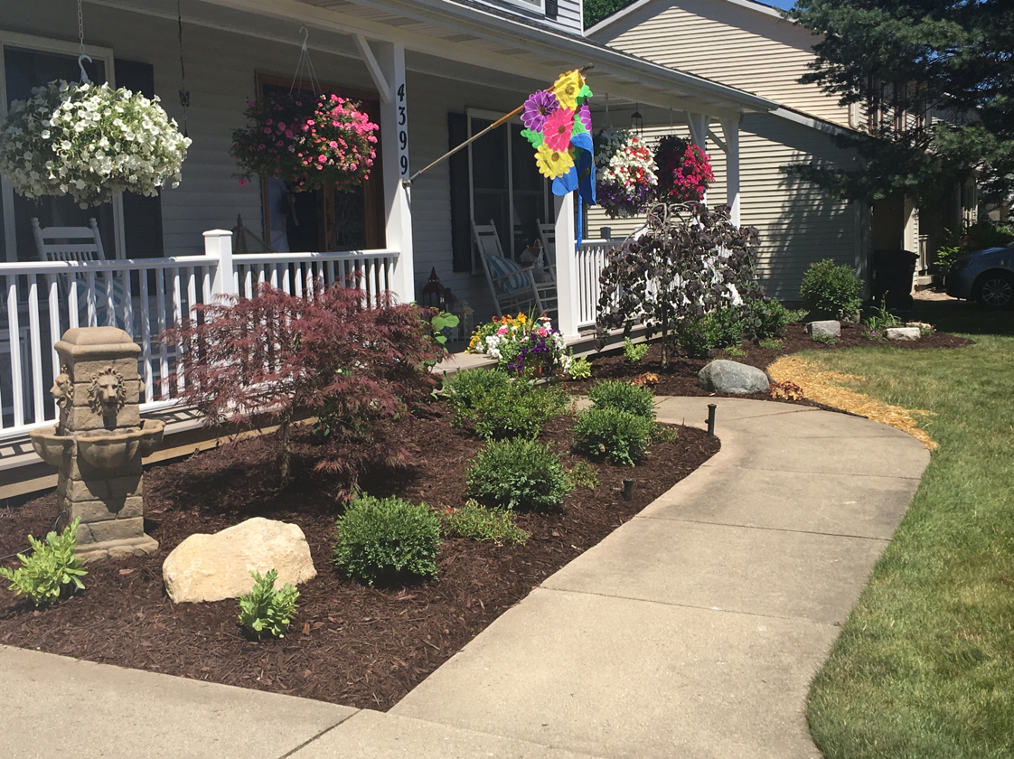 Front yard with porch, colorful flowers, stone fountain, and a landscaped garden bed.