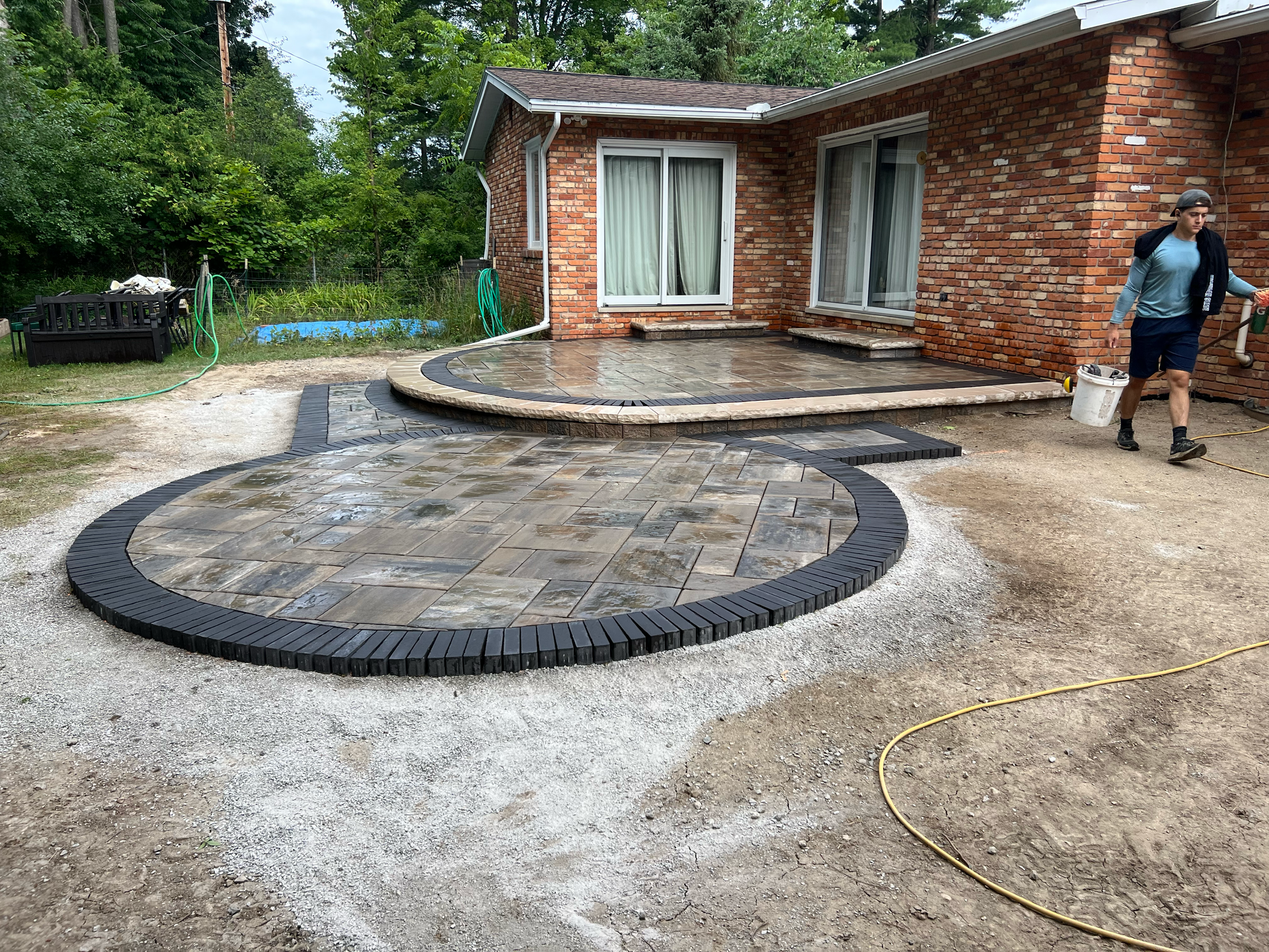 Brick home with a new stone patio and a person carrying a bucket.