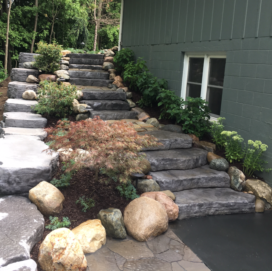 Stone steps with landscaping leading up to a green building with a window.