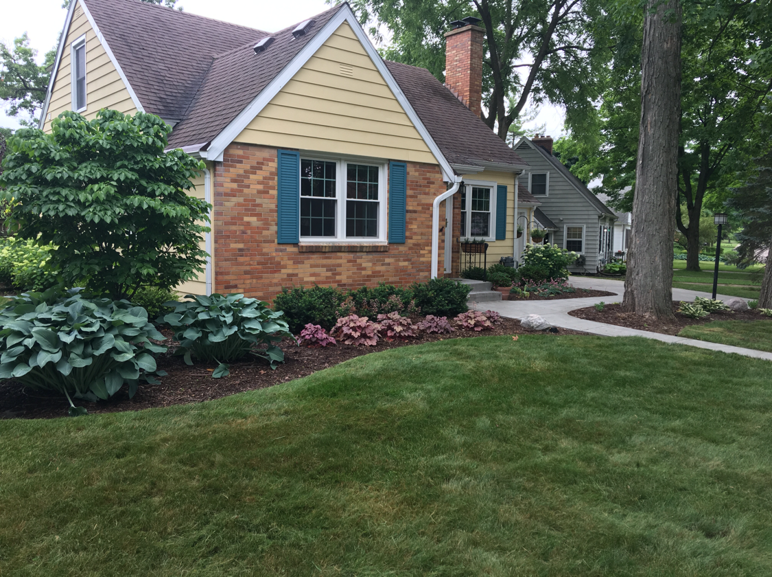 Yellow house with brick facade, blue shutters, and manicured lawn.