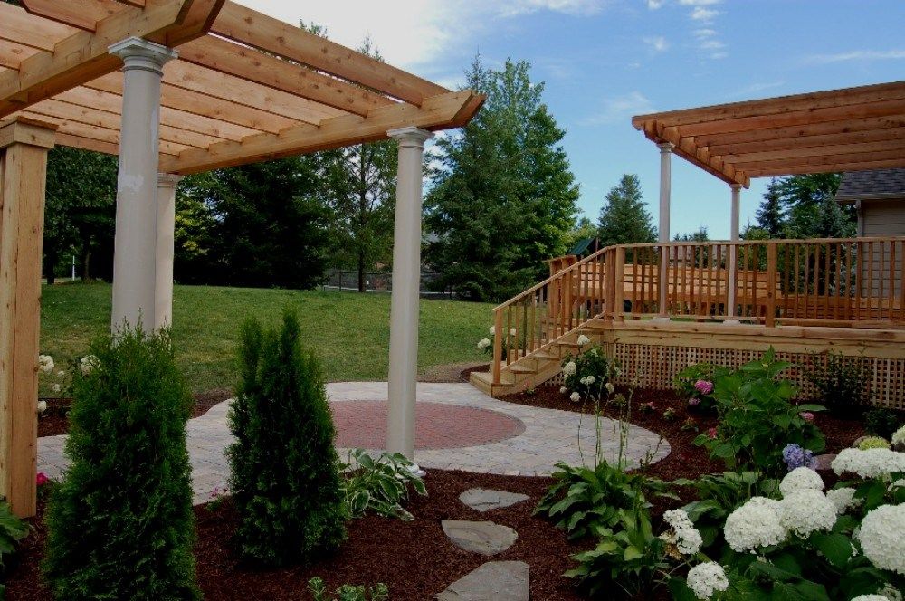 Pergola and deck in a landscaped backyard with a stone pathway and flower beds.