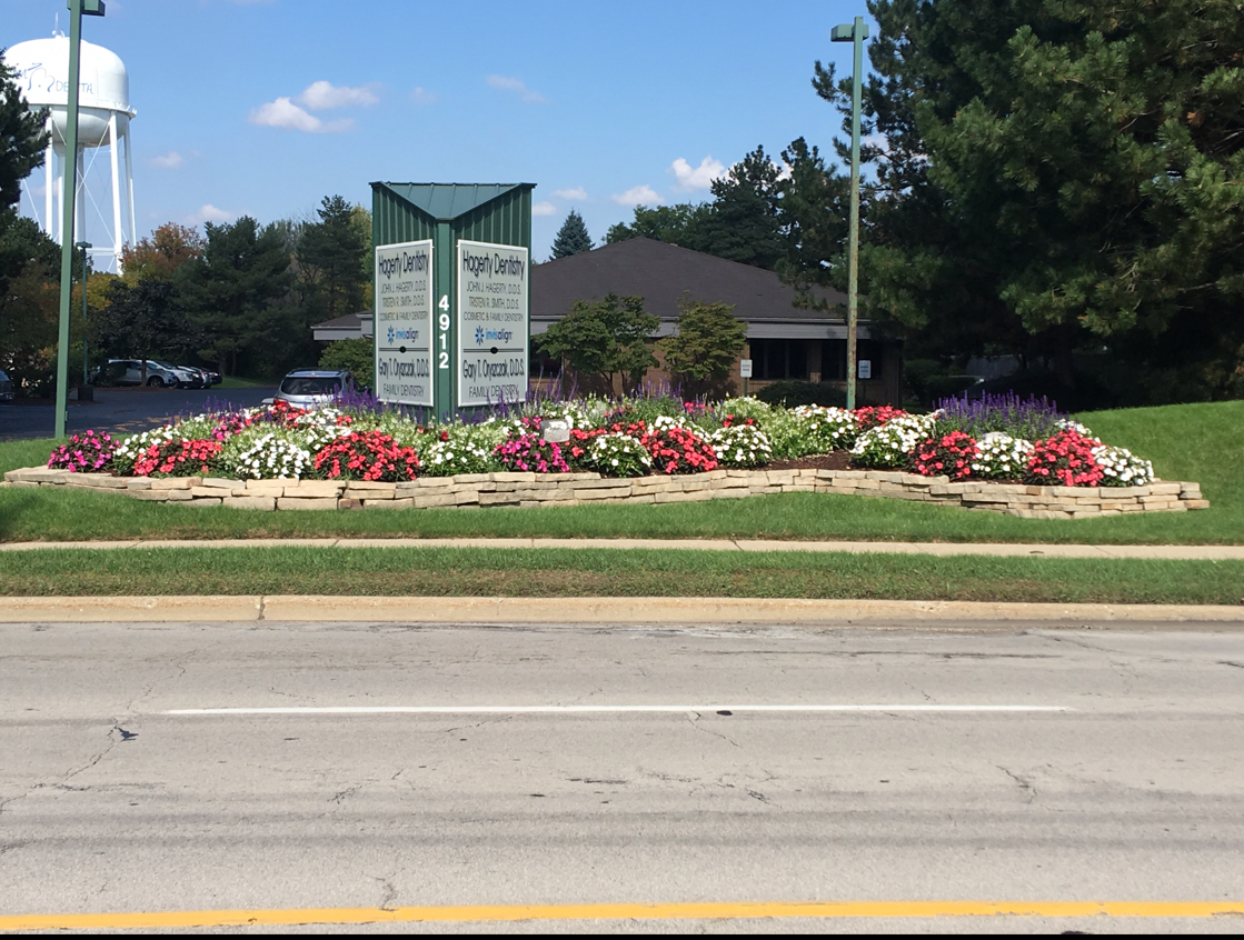 Sign for businesses surrounded by a flower bed with a water tower in the background.