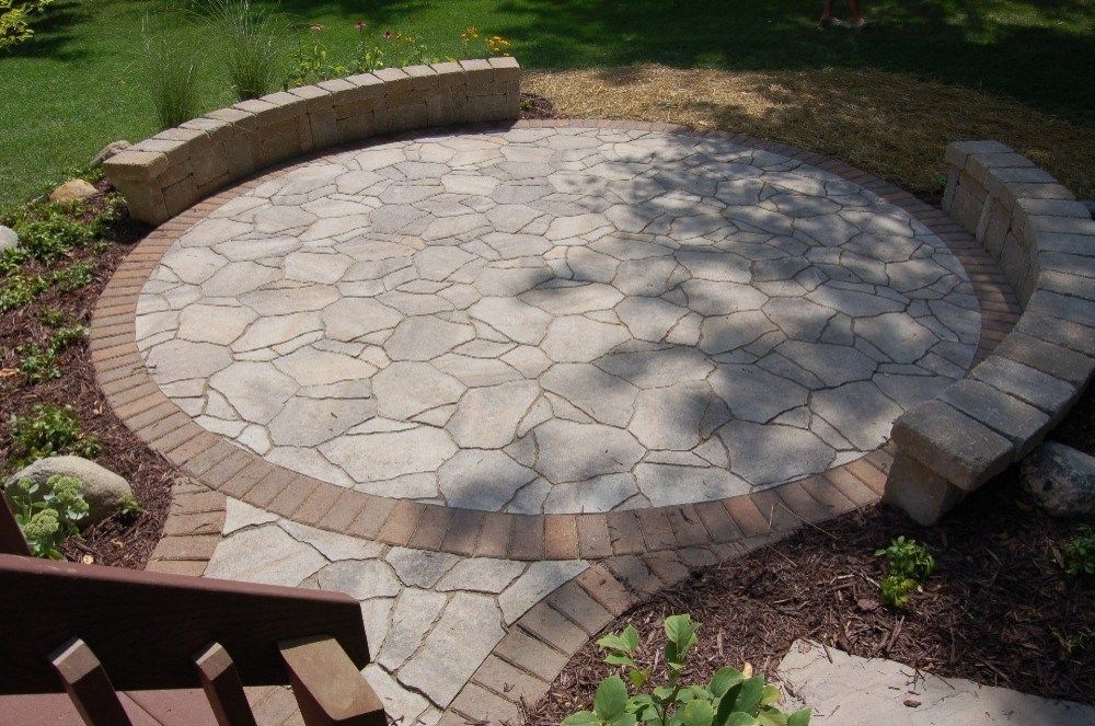 Circular stone patio with curved seating, surrounded by landscaping and garden edging.