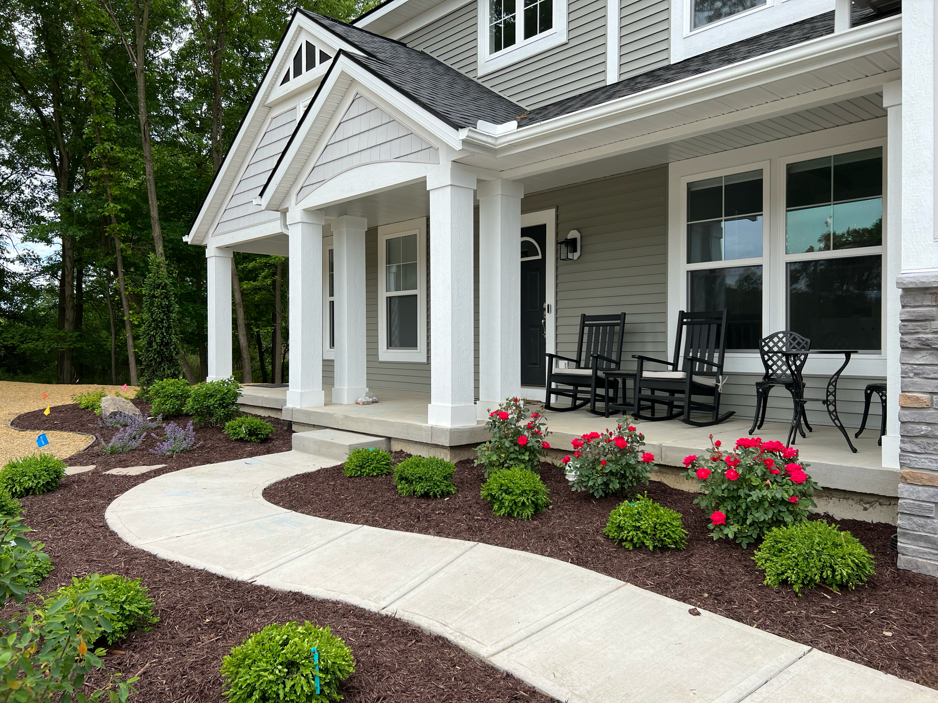 A house with a wraparound porch, a concrete walkway, and landscaped flowerbeds.