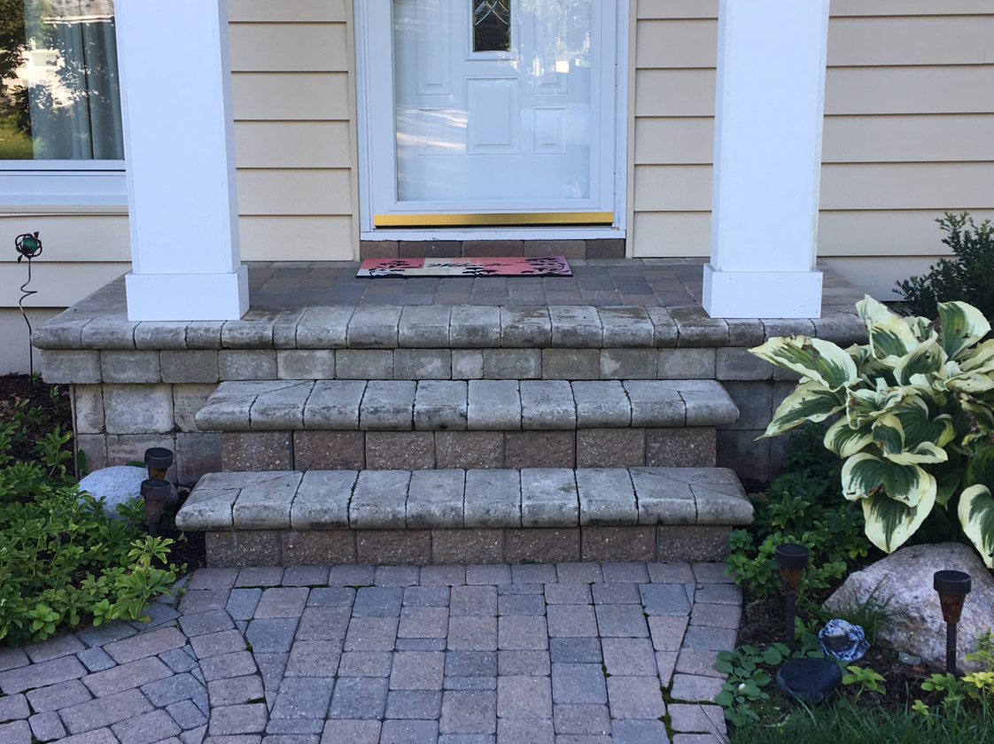 Stone steps leading up to a white front door. Beige siding, plants on either side.