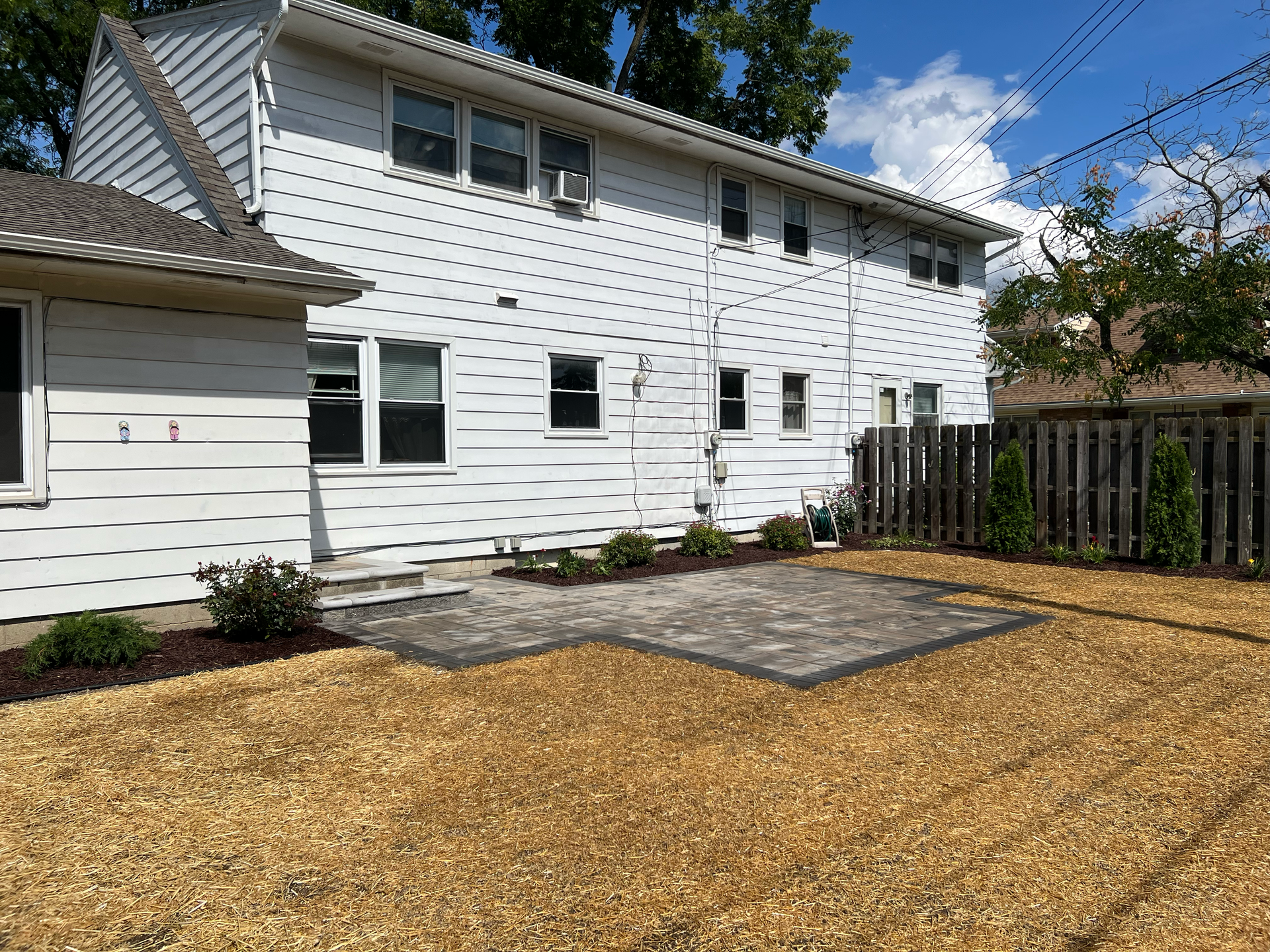 Backyard with white house, patio, wooden fence, and mulch ground covering.