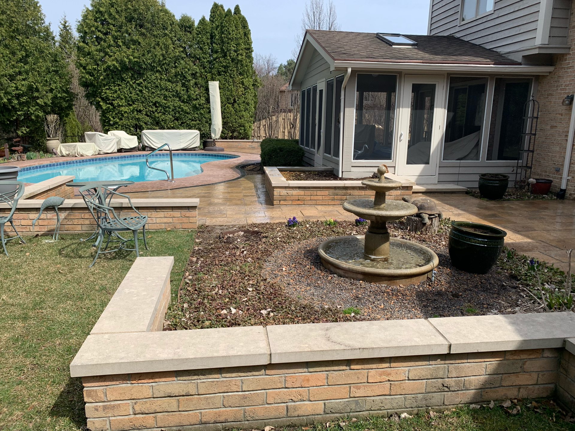 Backyard with pool, fountain, and sunroom. Brick retaining walls surround the garden beds.