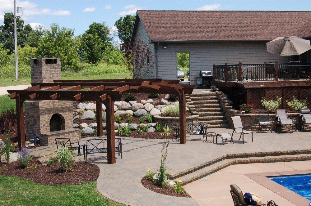Outdoor patio with fireplace, pergola, and pool near a house and deck.