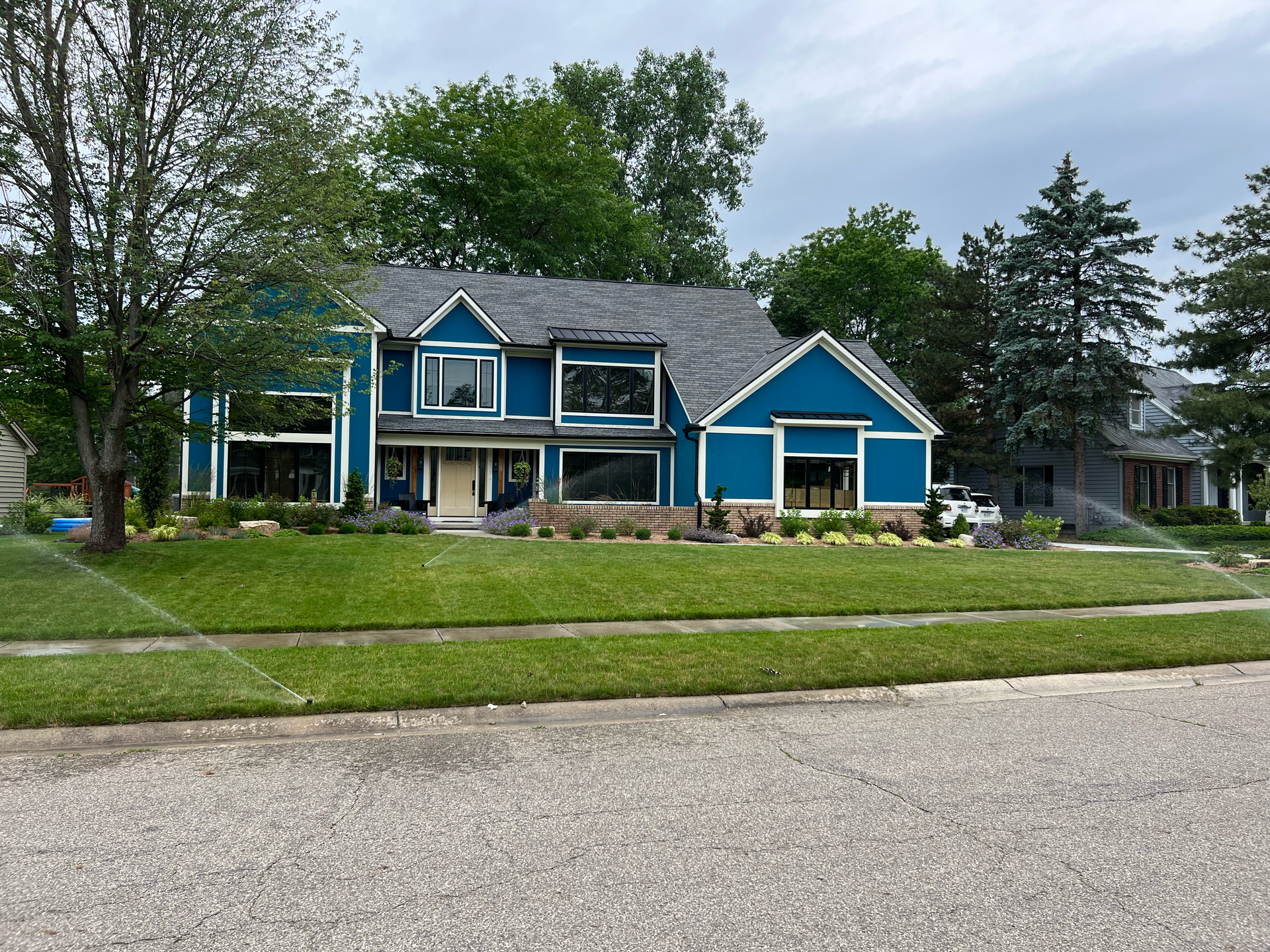 Blue house with large windows, set on a green lawn, and lined with trees.