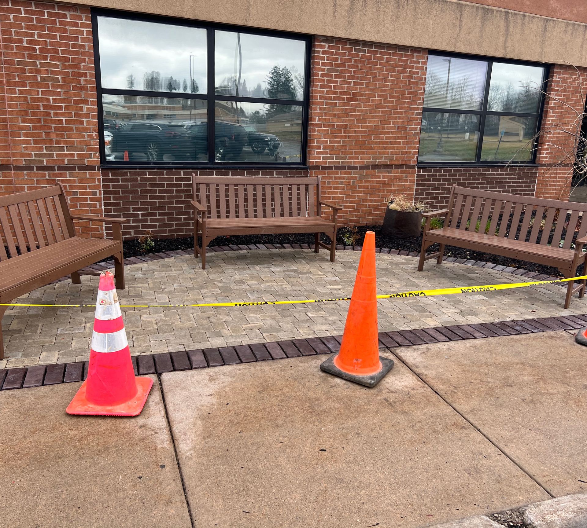 Outdoor area with brick building, benches, orange cones, and caution tape.