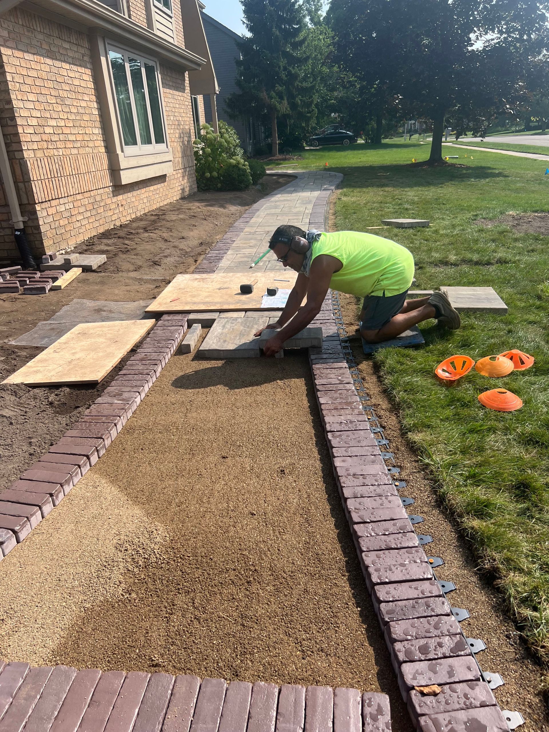 A worker installs paving stones on a walkway edged with red bricks.