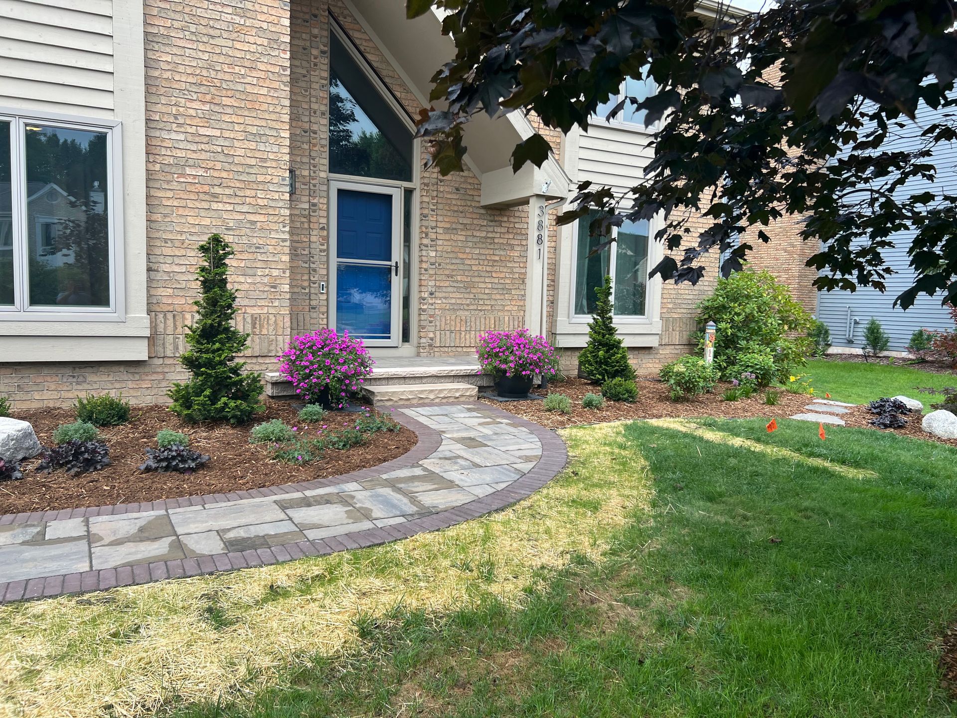 Brick house with stone path, trimmed bushes, and colorful flowers in a manicured lawn.