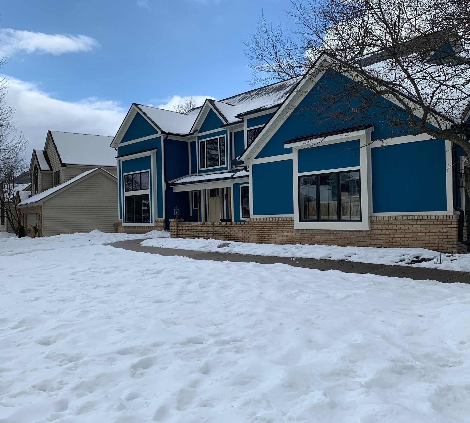 Blue house with white trim, covered in snow, under a blue sky.
