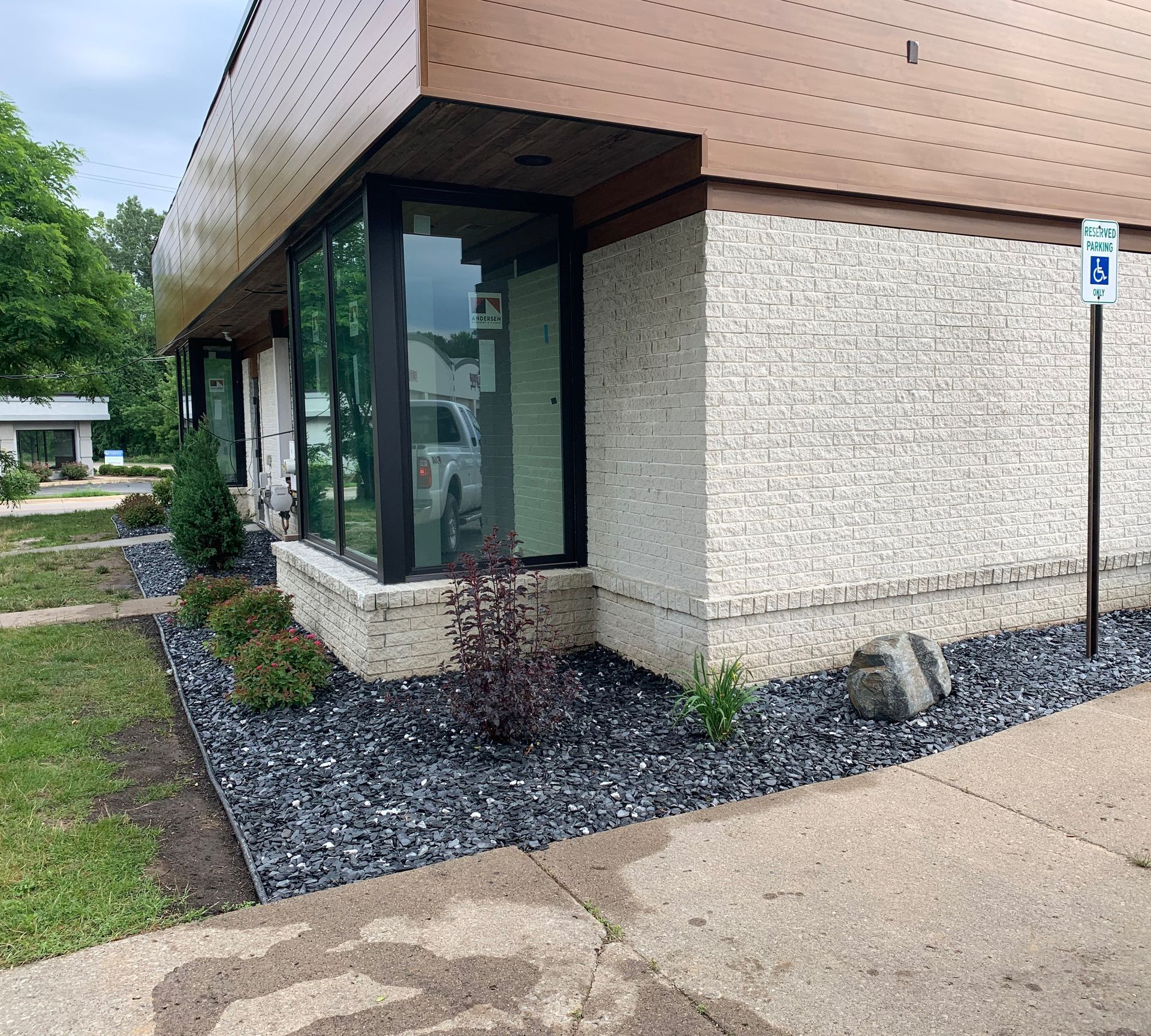 Exterior of a building with accessible parking sign. Dark mulch borders the building with bushes.