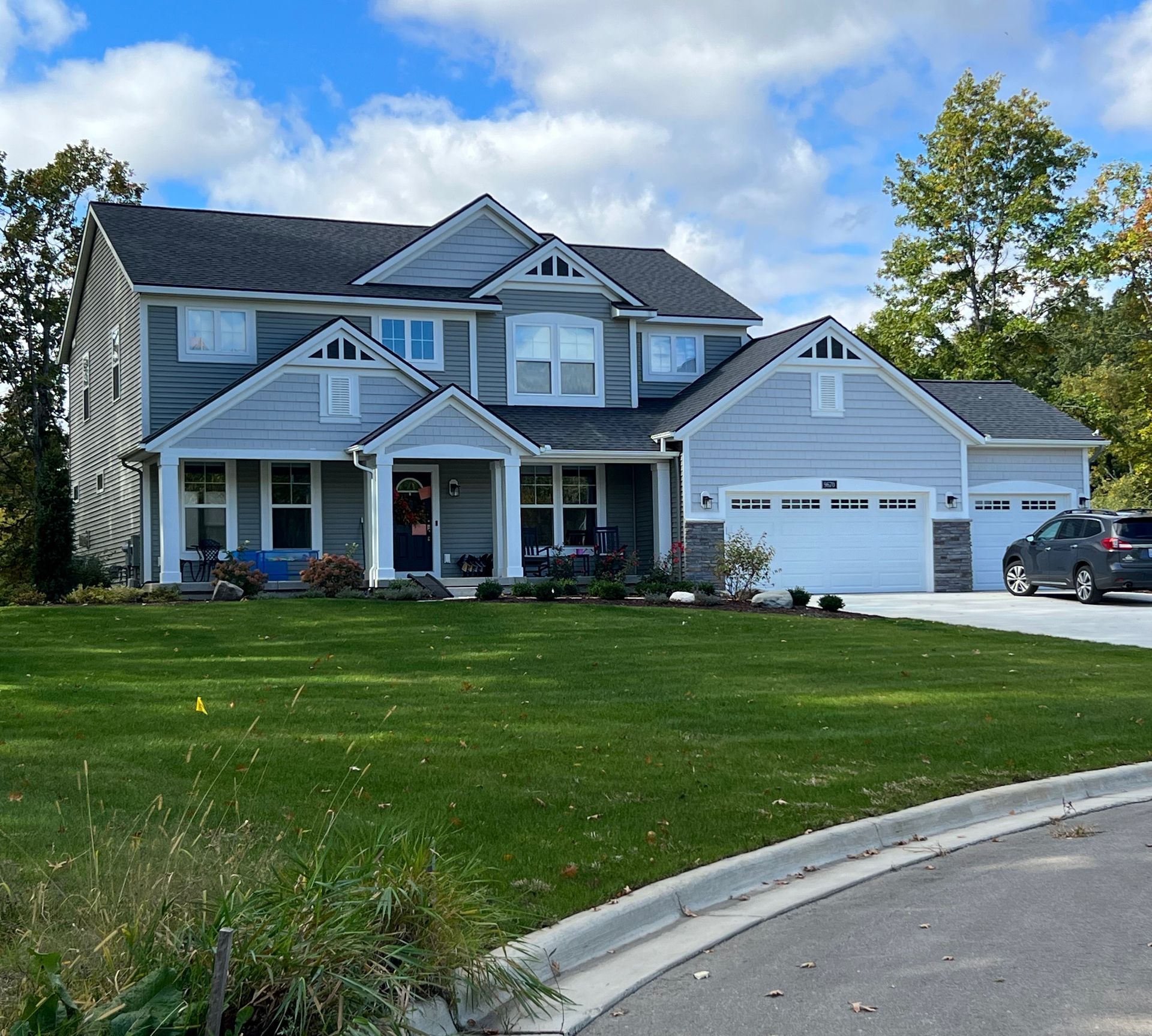 Two-story blue house with a three-car garage, white trim, and a well-kept green lawn on a sunny day.