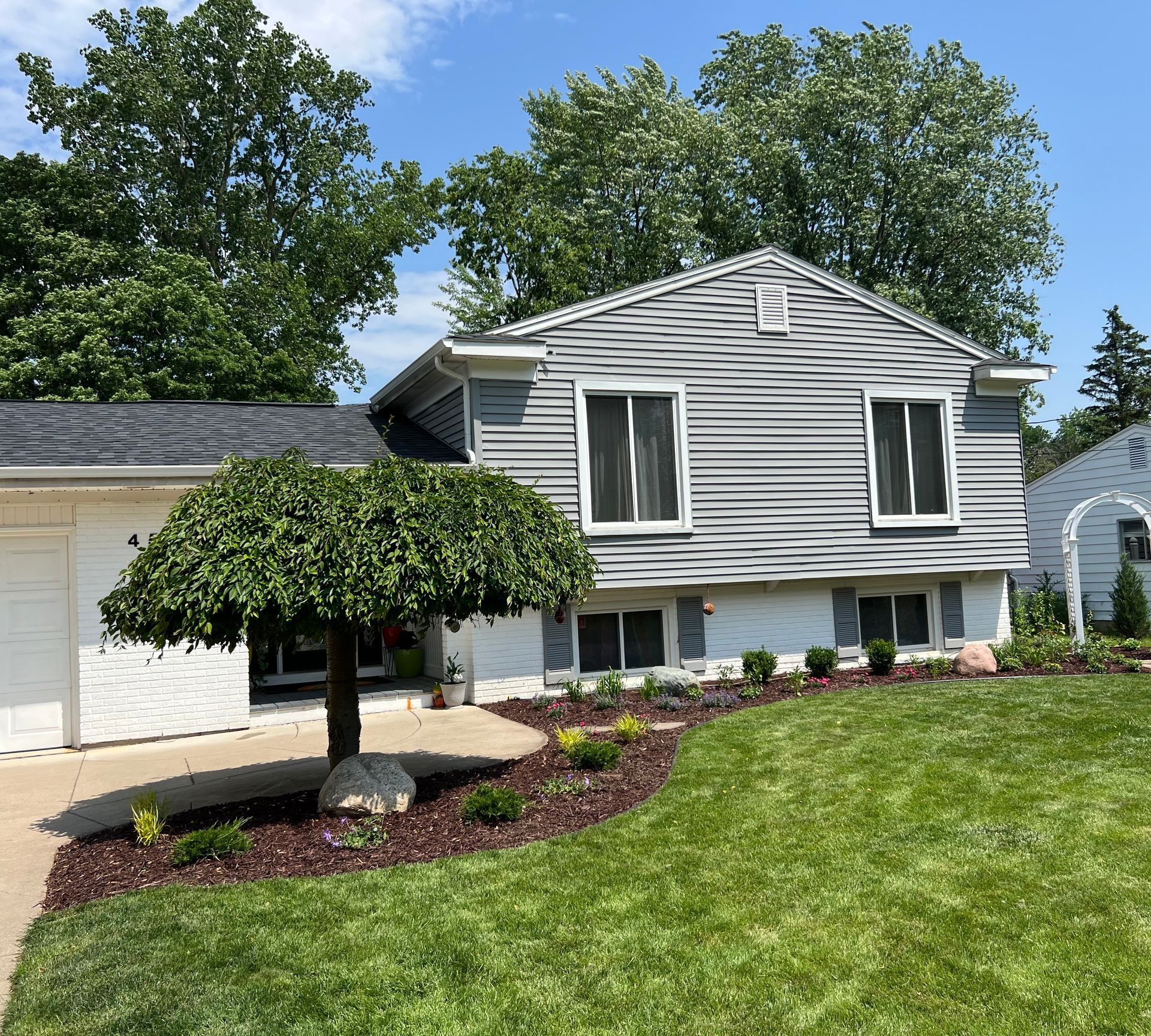 Gray house with landscaping and weeping tree in front yard.