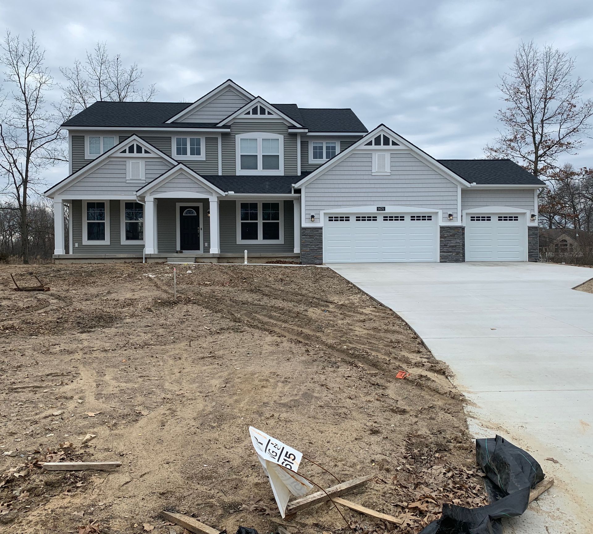 New light grey house with black roof, garage, and unfinished yard; concrete driveway.