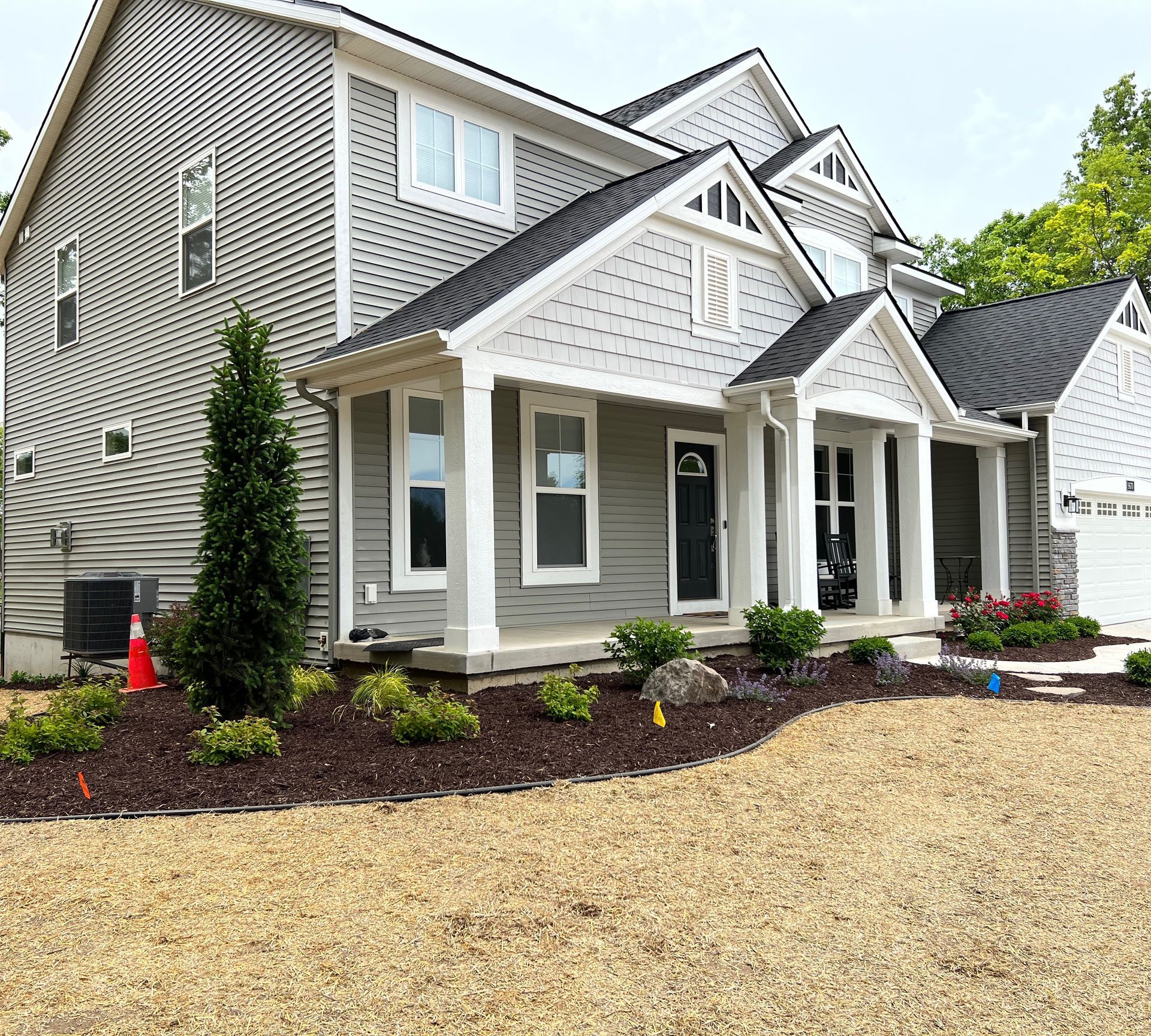 Gray house with white trim, front porch, and black front door; landscaping in front.