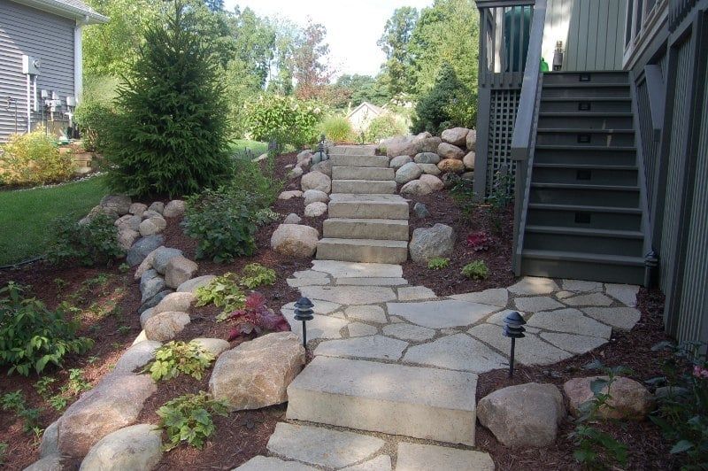 Stone steps and pathway lead up a landscaped hillside with boulders and plants.