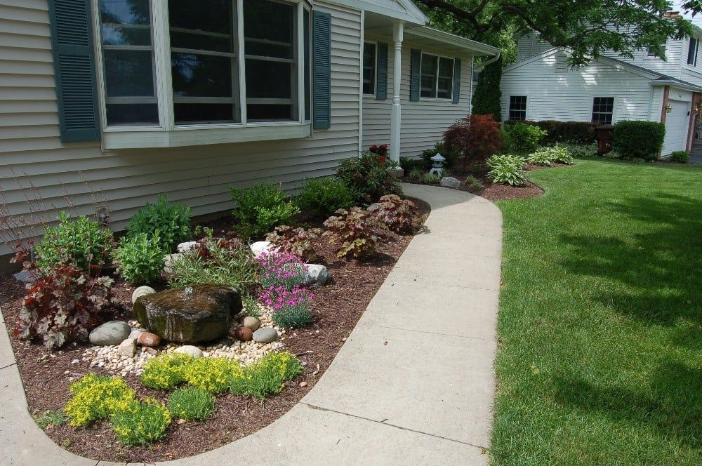 Front yard with a flower bed bordering a curved walkway leading to a house.
