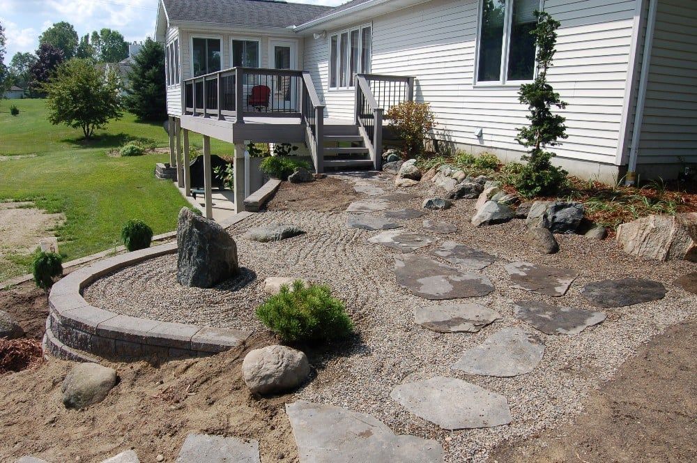 Stone pathway and rock garden next to a house with a deck.