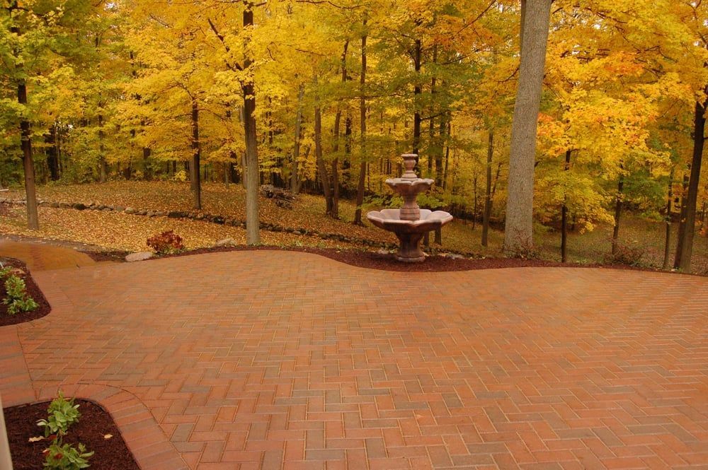 Brick patio with a fountain, surrounded by trees with yellow autumn leaves.