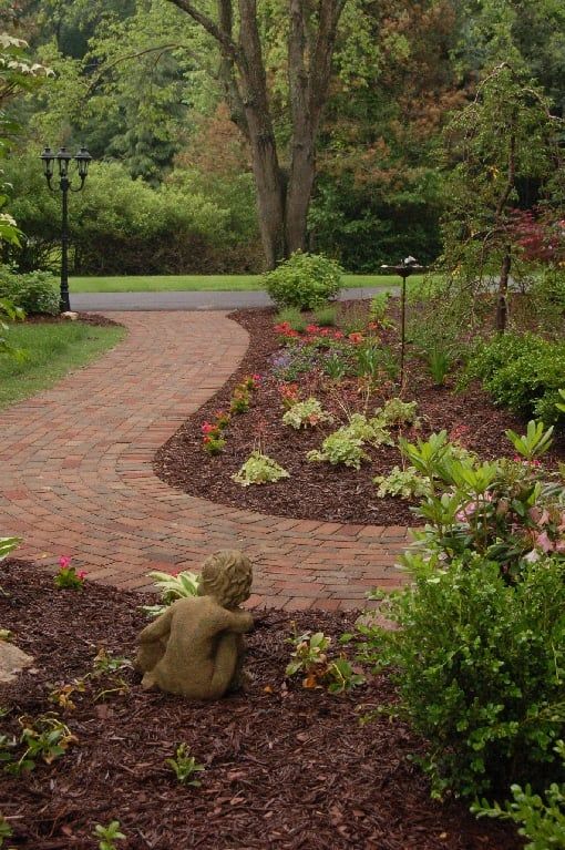 Brick pathway curves through a garden with a statue of a small child and various plants.