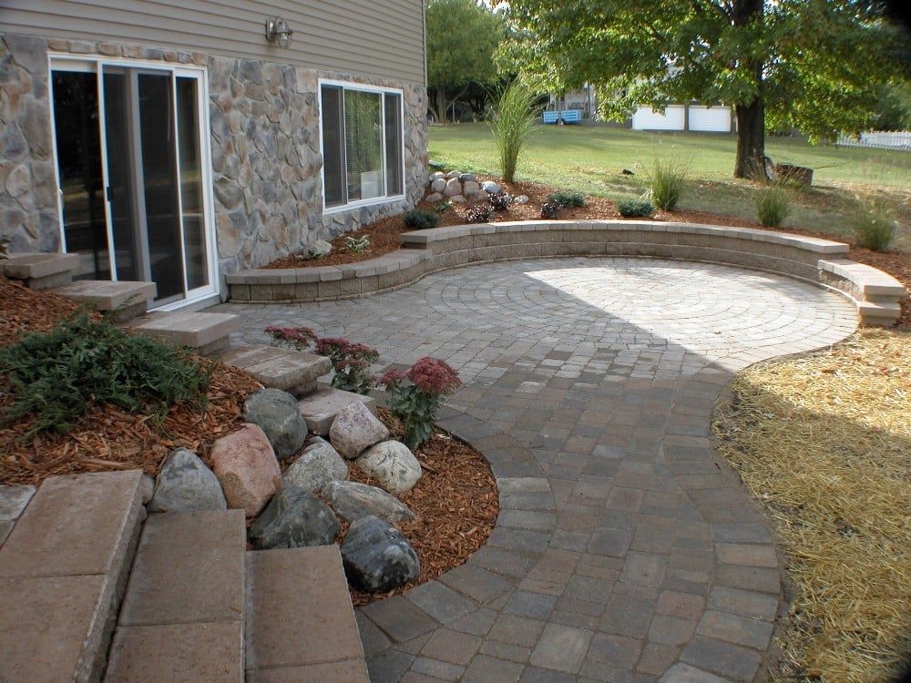 Stone patio and retaining wall by a house, with steps, landscaping, and a grassy yard.