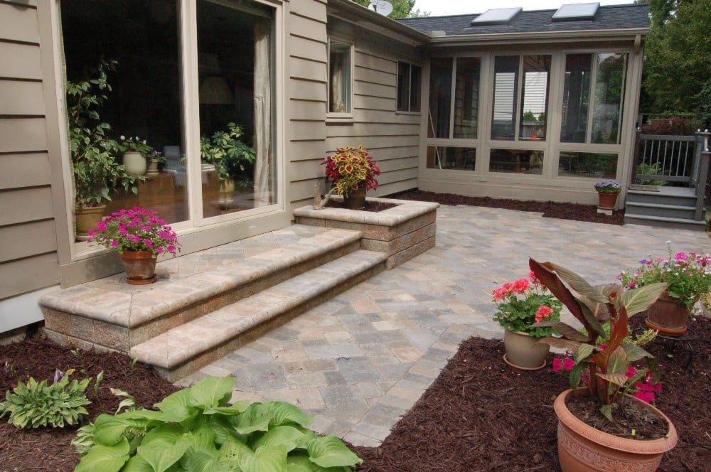 Stone patio with steps leading to a sliding glass door. Flower pots surround the patio.