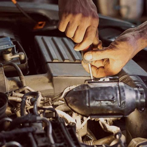 A man is working on a car engine with a screwdriver.