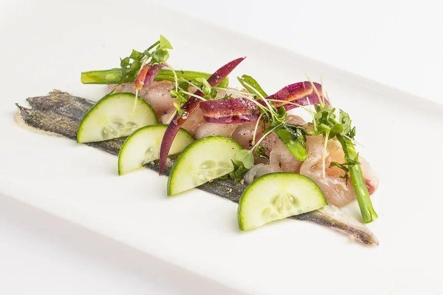 piatto con pesce bianco crudo, cipolle rosse e cetrioli