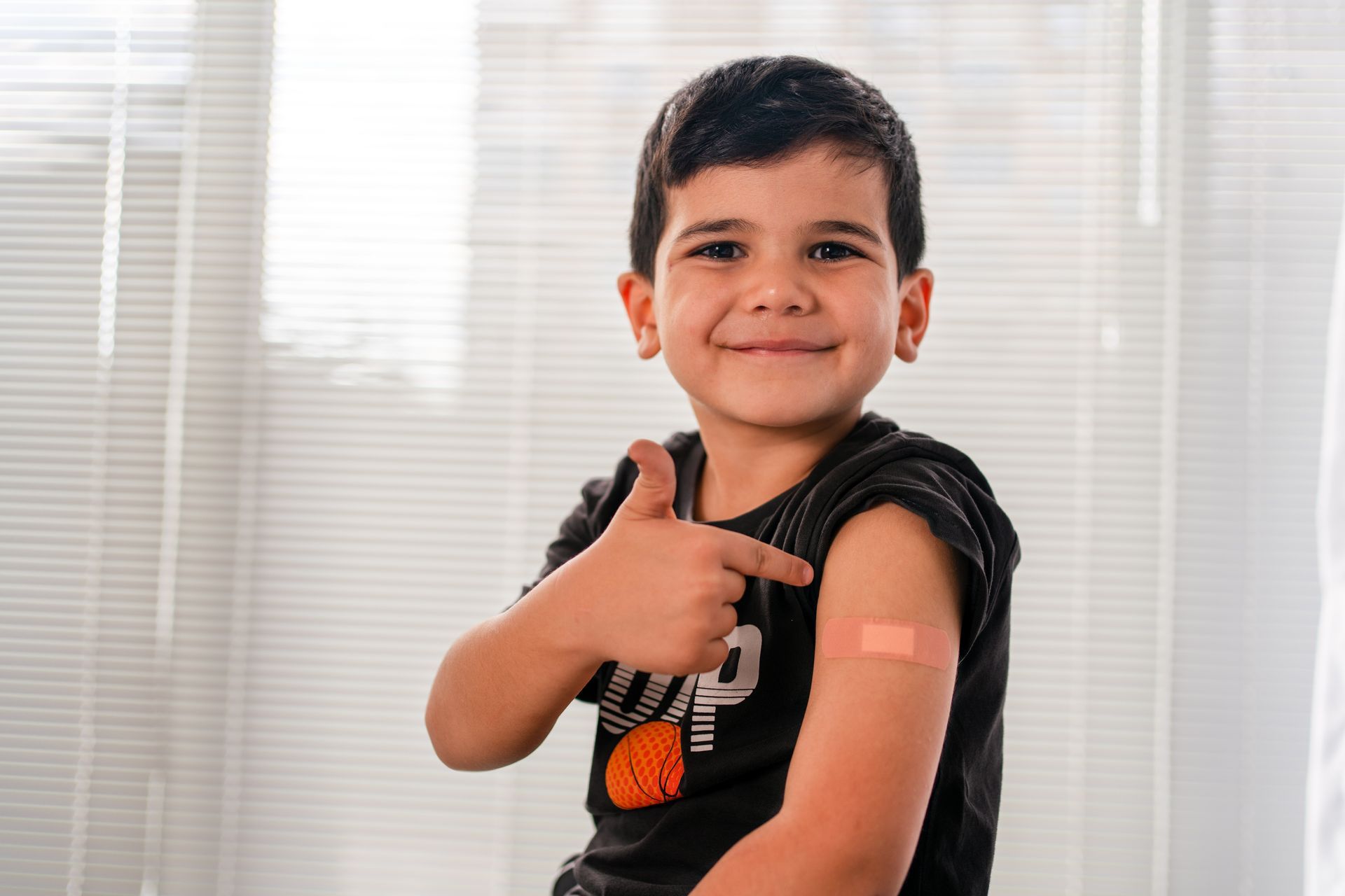 A young boy is pointing at his arm with a bandage on it.