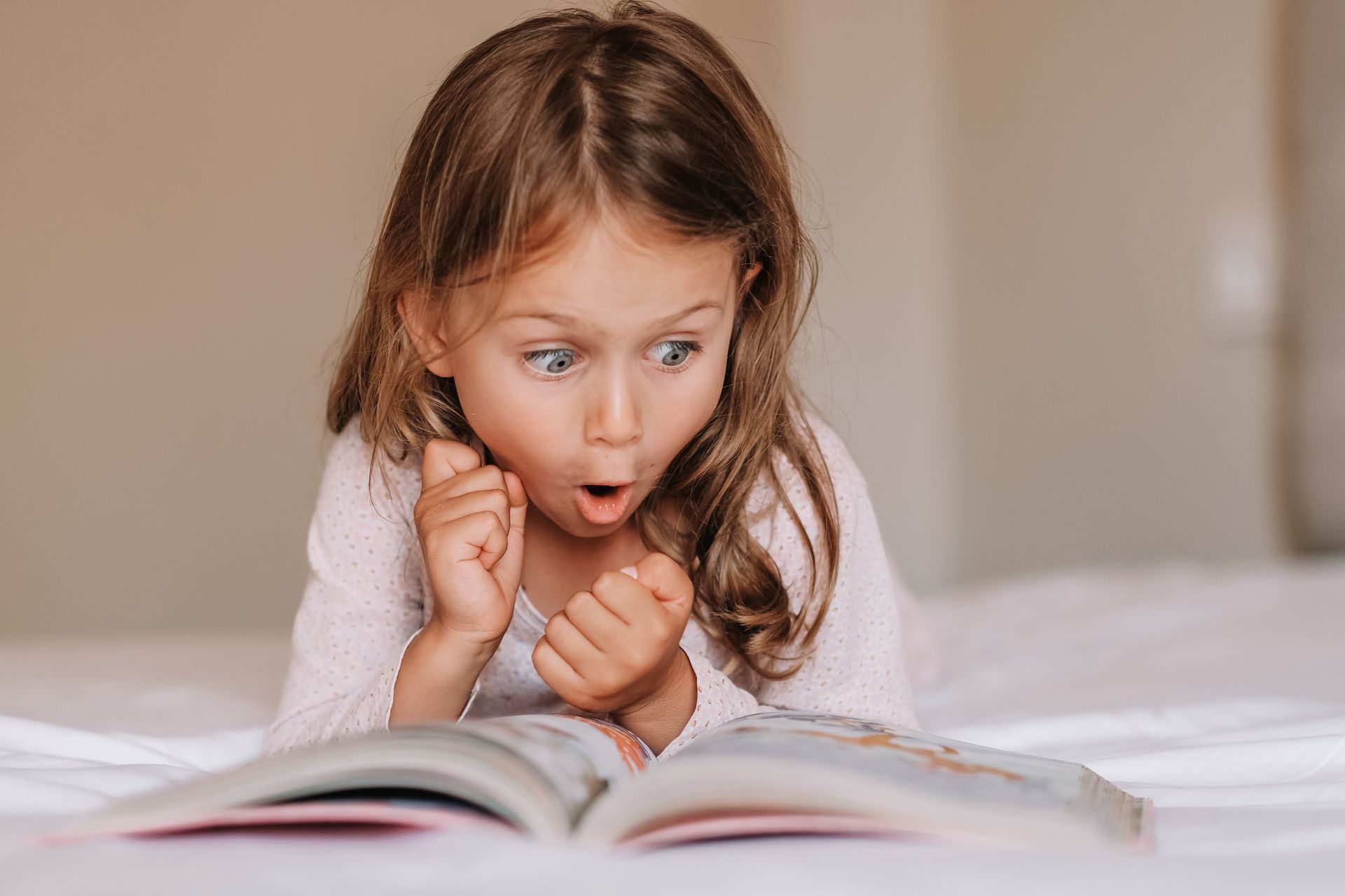A little girl is laying on a bed reading a book.
