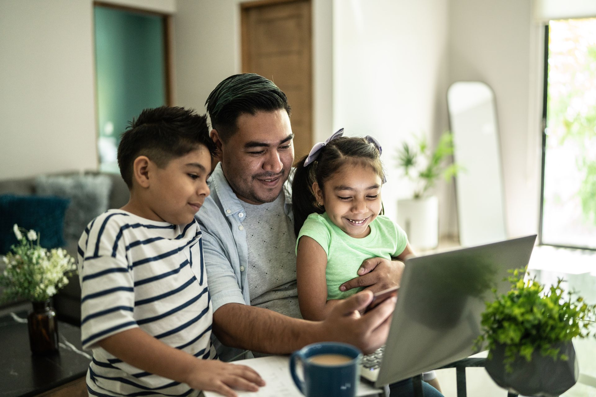 A man and two children are sitting at a table looking at a laptop.